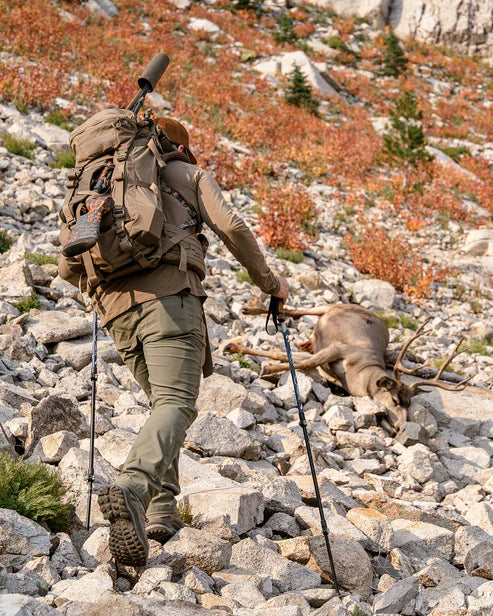 Ausgerüstet mit dem EBERLESTOCK Brute 3500 Rucksack und Trekkingstöcken klettert ein Wanderer einen felsigen Berghang hinauf, um ein gefallenes Reh in kargem Terrain zu finden, und fängt damit die Essenz eines Outdoor-Abenteuers ein.
