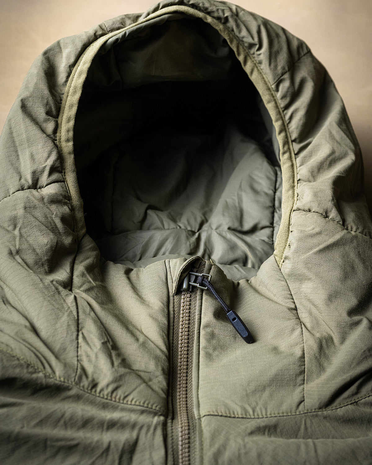 Die EBERLESTOCK Alturas Hooded Jacket in Dry Earth zeichnet sich durch einen sichtbaren Frontreißverschluss und ein offenes Design aus, um das Innenfutter zu zeigen, das sich auf einem neutralen Hintergrund präsentiert - ideal als Outdoor-Jacke oder Jagdjacke.