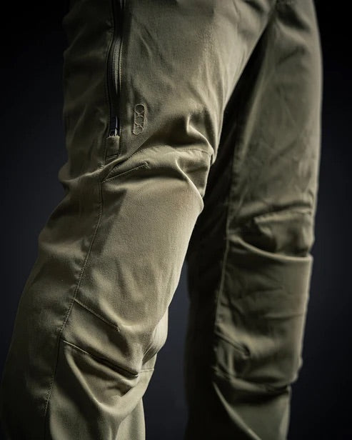 Nahaufnahme einer Person, die die EBERLESTOCK Camas Pro Pant in Coyote Brown trägt, mit Reißverschlusstaschen und vorgeformten Knien, vor einem dunklen Hintergrund.