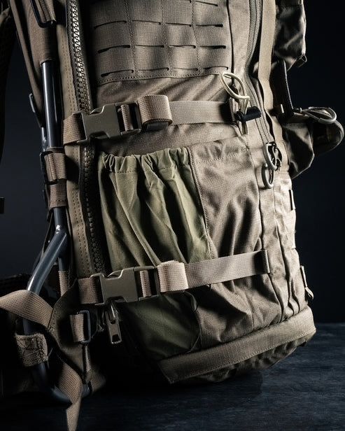 Eine Nahaufnahme des taktischen Rucksacks Mission Ruck von EBERLESTOCK mit robustem Material, MOLLE-Gewebe, mehreren Riemen, Schnallen und Taschen vor einem dunklen Hintergrund.