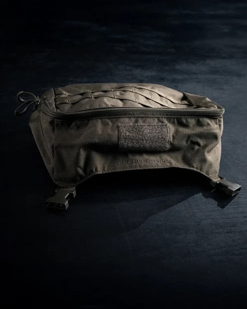 Der EBERLESTOCK Mission Ruck, eine dunkelgrüne taktische Tasche mit Reißverschluss, Tragegriff und zwei Bodenschnallen, wird auf einer dunklen Fläche unter dramatischer Beleuchtung präsentiert.