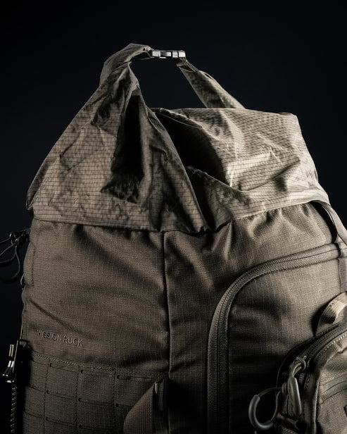 Nahaufnahme des taktischen Rucksacks Mission Ruck von EBERLESTOCK in Grau mit strukturiertem Stoff, mehreren Reißverschlussfächern und einem Griff mit Klappe an der Oberseite vor einem dunklen Hintergrund.