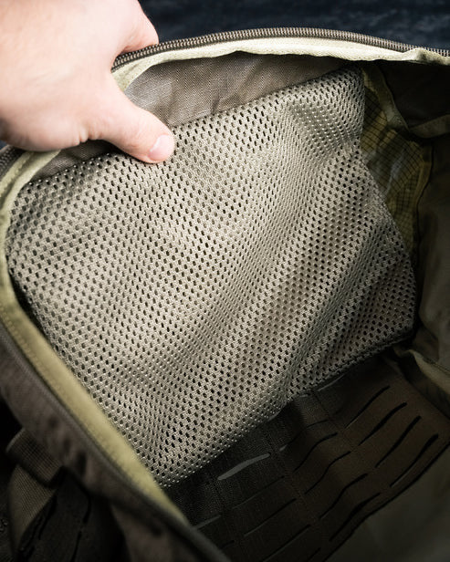 Eine Hand öffnet den oberen Reißverschluss eines olivgrünen EBERLESTOCK Mission Rucksacks und gibt den Blick auf ein Netzinnenfach im Hauptfach dieses vielseitigen Rucksacks frei.