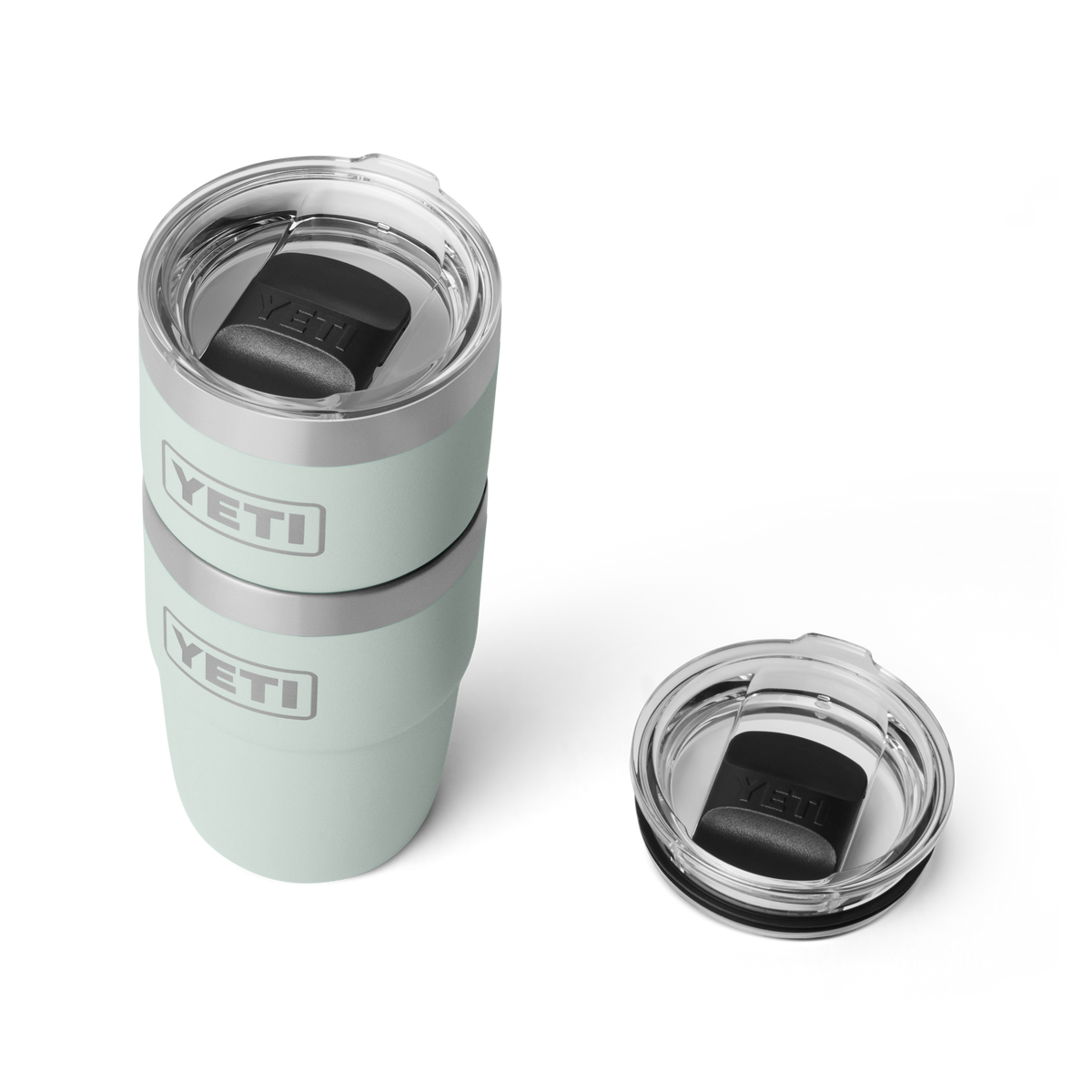 Zwei hellgrüne YETI® Stapelbarer Becher Rambler 8 Oz - Ridgeline sind gestapelt, jeder mit einem durchsichtigen Kunststoffdeckel mit schwarzem Schiebeverschluss. Ein dritter identischer Deckel liegt rechts auf weißem Hintergrund.