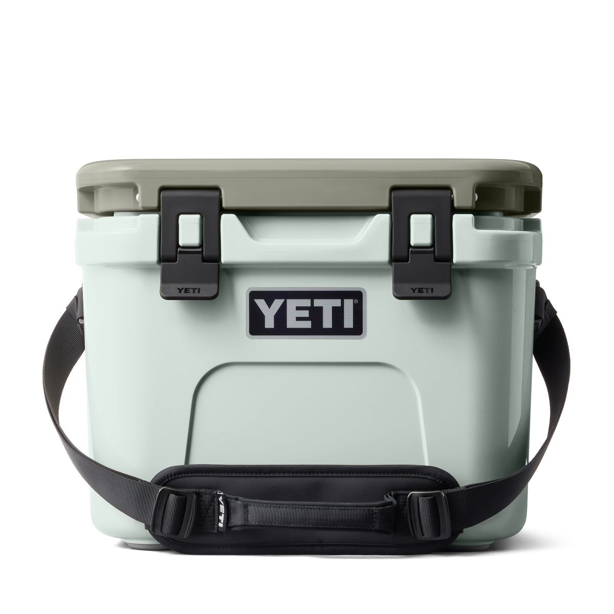 Eine hellgraue YETI® Kühlbox Roadie 15 - Ridgeline mit salbeigrünem Deckel, schwarzen Seitenverschlüssen und Schultergurt sowie dem YETI-Logo auf der Vorderseite.