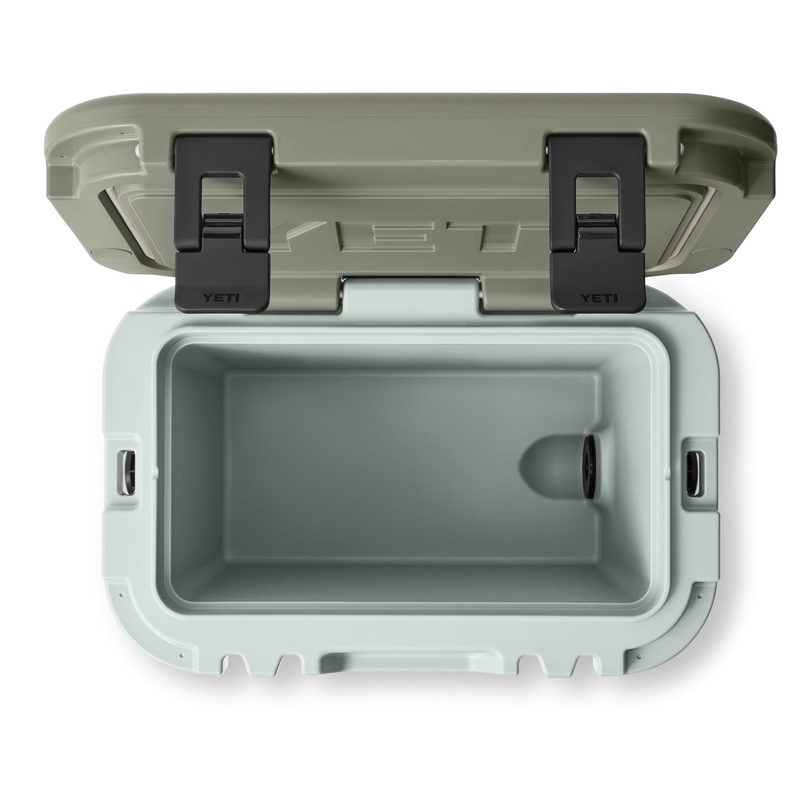 Draufsicht auf eine geöffnete YETI® Kühlbox Roadie 15 - Ridgeline mit hellgrünem Innenraum, hellbraunem Deckel, zwei schwarzen Verschlüssen und einer Ablassschraube an der rechten Seite. Die Kühlbox ist leer. Marke: YETI.