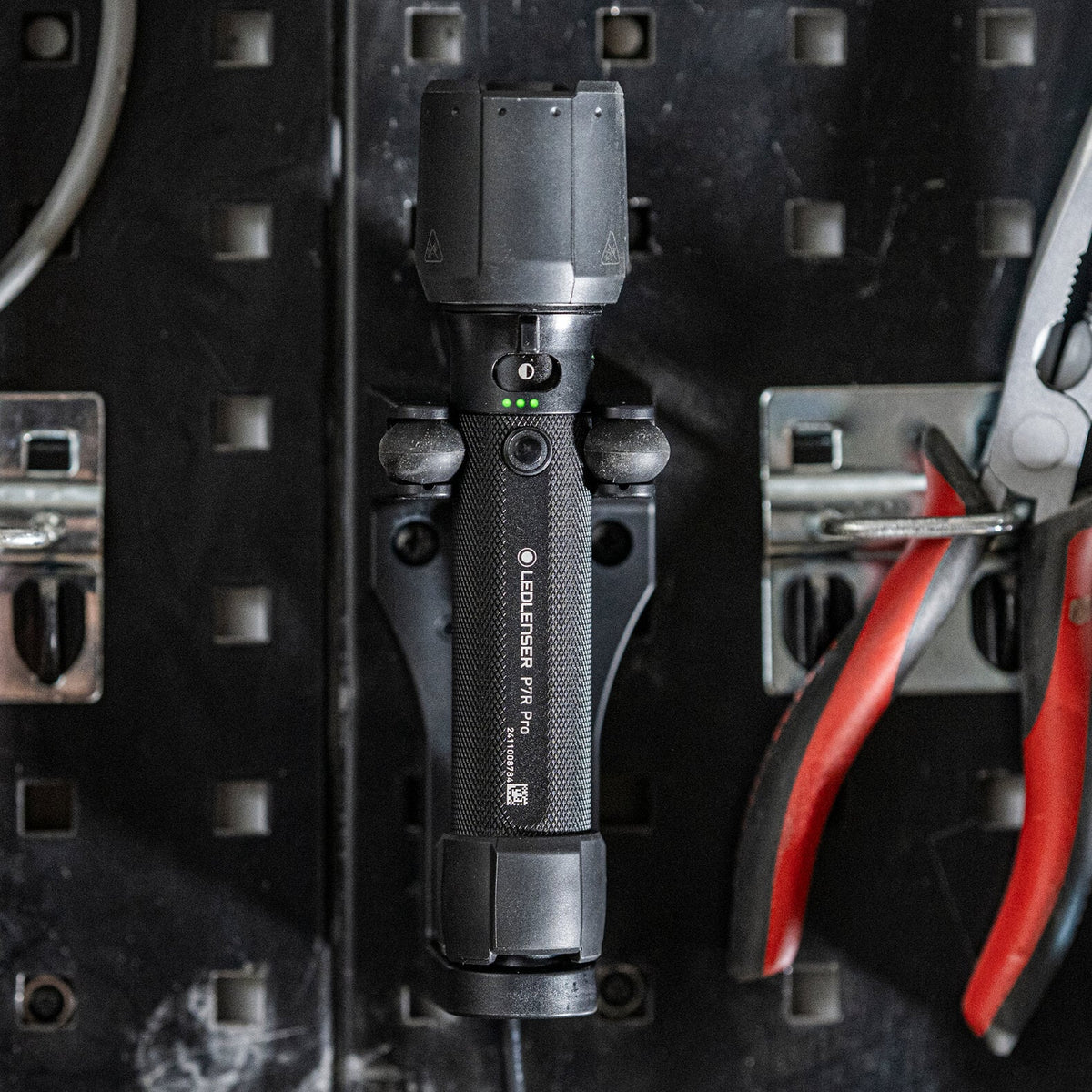 Eine schwarze LEDLENSER Taschenlampe P7R Pro ist senkrecht auf einem Lochblechbrett montiert, flankiert von einer rot lackierten Zange und einem grauen Kabel.