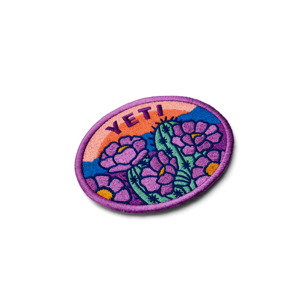 Das YETI® Full Bloom Patch von YETI zeigt lilafarbene Blumen, grüne Kakteen und "YETI" auf einem orange-rosa Sonnenuntergang mit lilafarbenem Rand und Klettbefestigung zur einfachen Befestigung an Ihrer Outdoor-Ausrüstung.