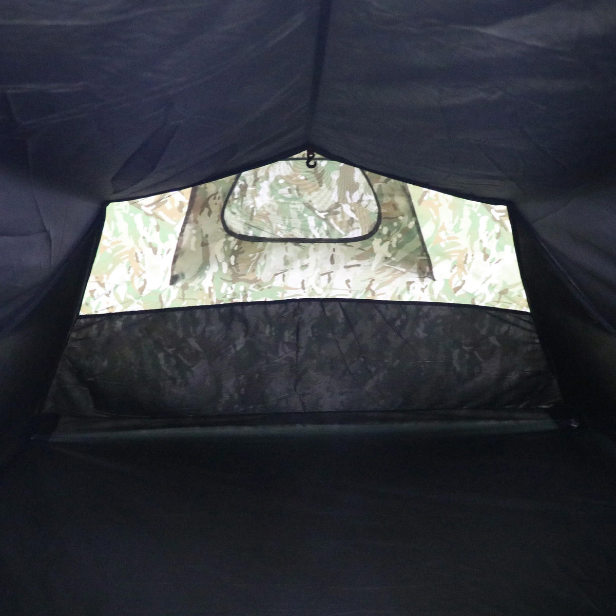Innenansicht des Highlander Zelt BLACKTHORN 2 GEN2 - HMTC von HIGHLANDER FORCES mit einem Eingang mit Tarnmuster, einem schwarzen Netzgitter und einfallendem Licht - ein Kontrast zwischen dem dunklen Innenraum und dem hellen Äußeren dieses 2-Personen-Zeltes.