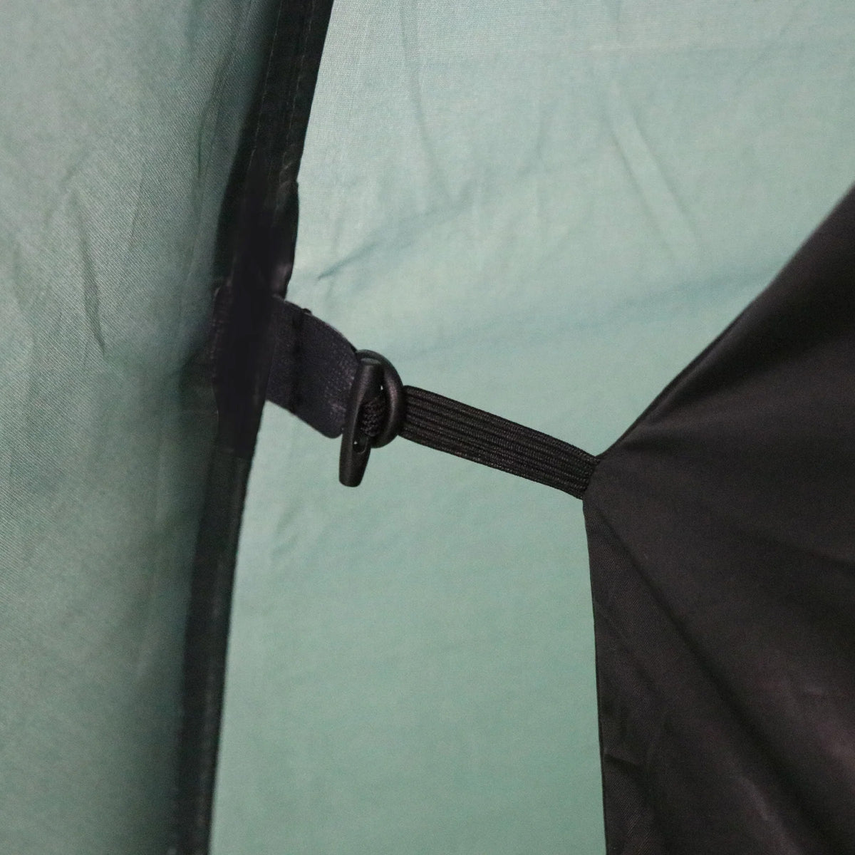 Nahaufnahme eines schwarzen Riemens und eines Kunststoffhakens, mit denen eine schwarze Klappe im Inneren des hellgrünen HIGHLANDER FORCES Highlander Zelt BLACKTHORN 2 GEN2 befestigt wird, die Teil der Innenstruktur des Trekkingzelts ist.