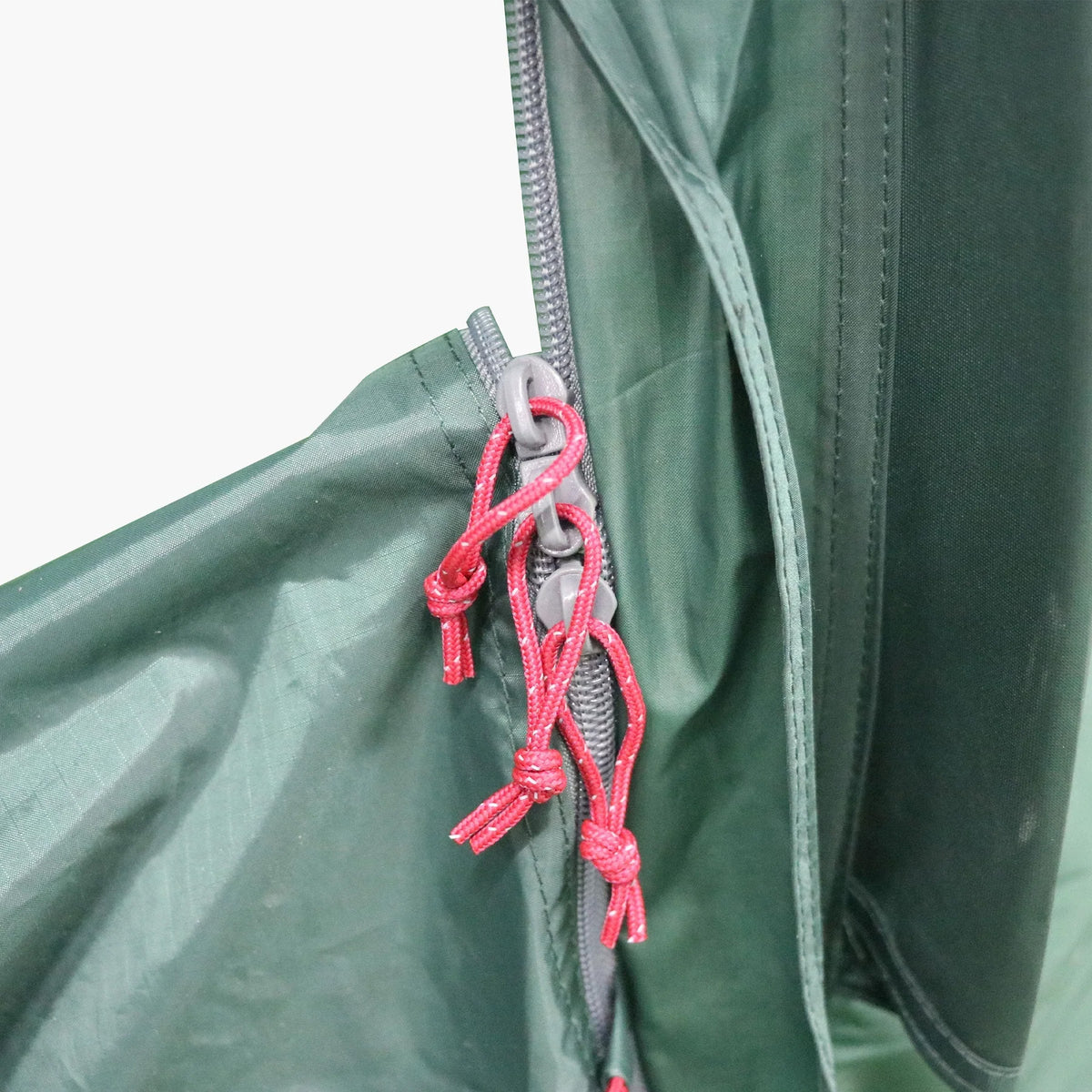 Nahaufnahme des HIGHLANDER FORCES Highlander Respite 2 Personen Extended Tunnelzelt - Pine Green Stoff, zeigt einen Reißverschluss mit drei roten Kordeln, die an den Zugbändern befestigt sind und die Zeltklappe sichern.