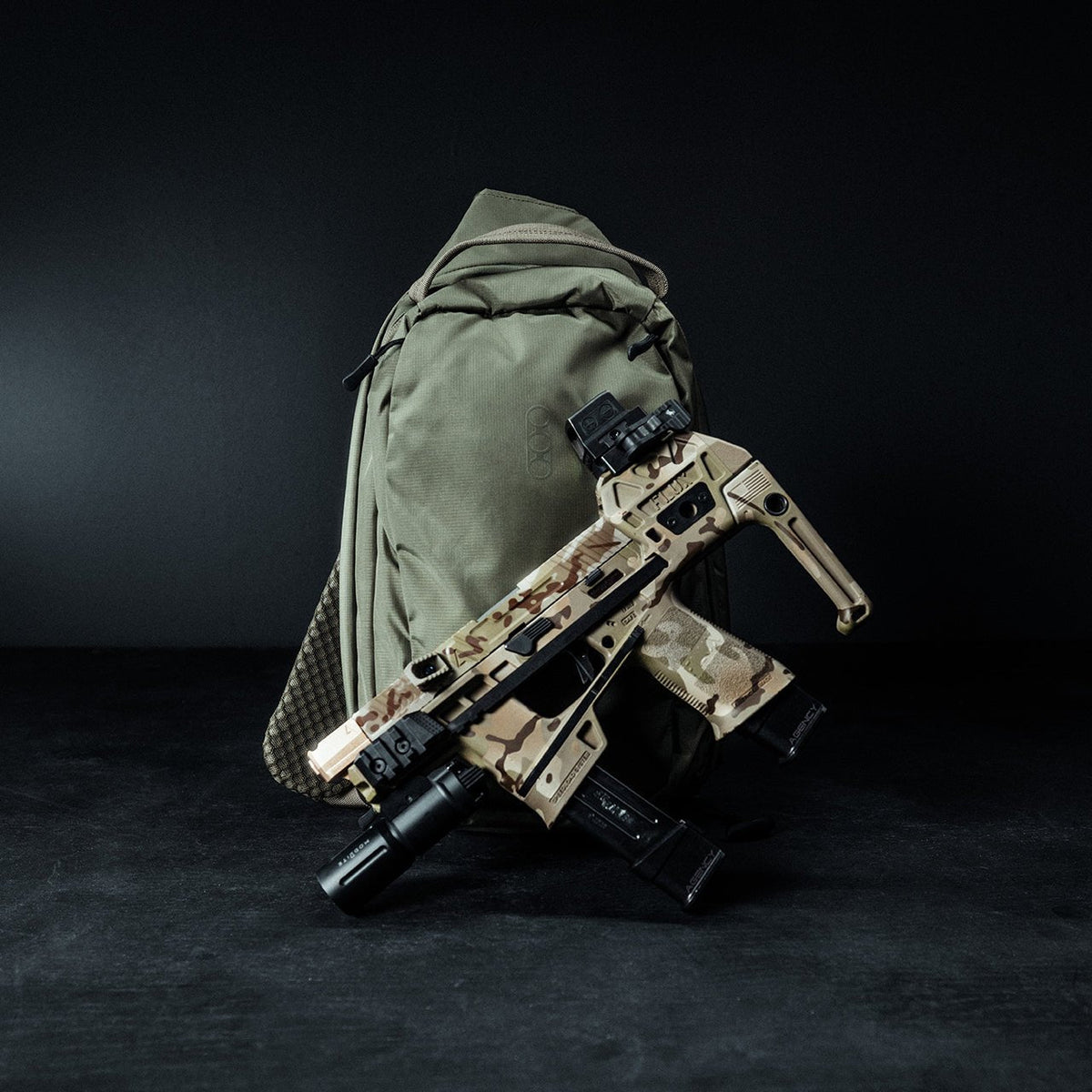 Auf dem olivgrünen EBERLESTOCK Eberlestock Fade Sling Rucksack ruht vor dunklem Hintergrund eine Schusswaffe mit Camouflage-Muster und Zubehör.
