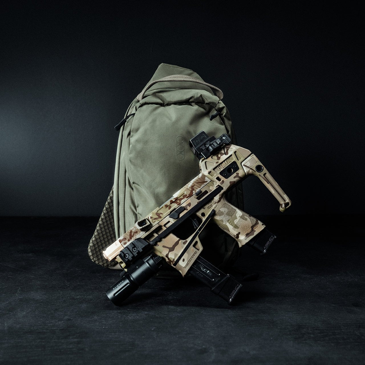 Auf dem olivgrünen EBERLESTOCK Eberlestock Fade Sling Rucksack ruht vor dunklem Hintergrund eine Schusswaffe mit Camouflage-Muster und Zubehör.