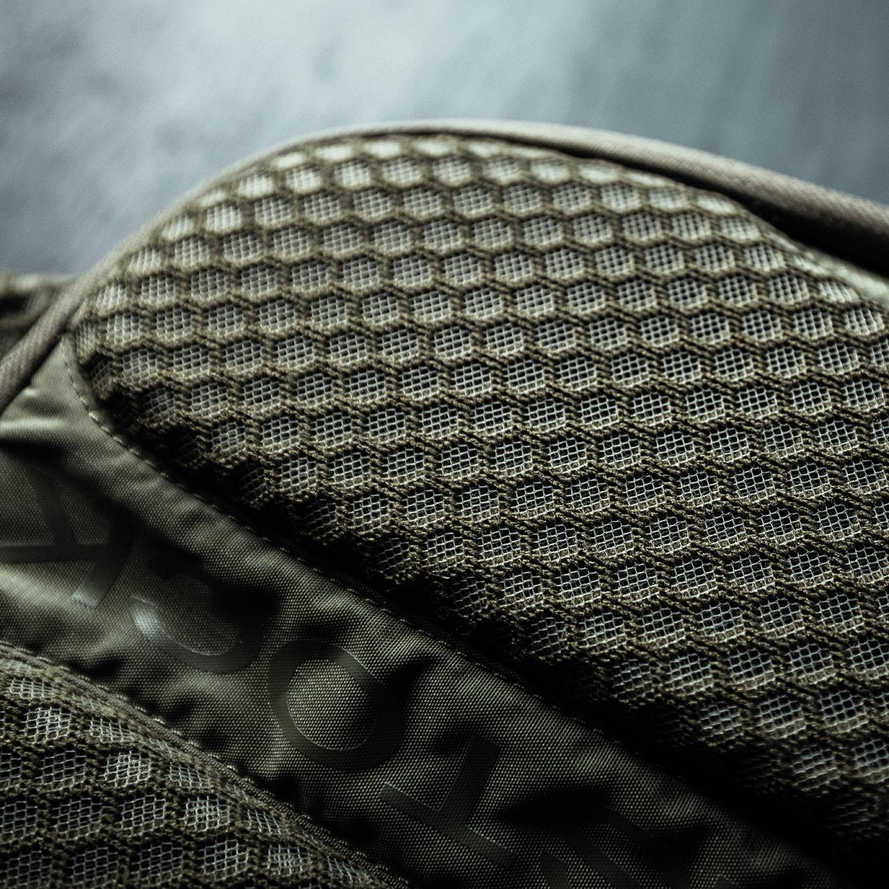 Nahaufnahme eines strukturierten dunkelgrauen Stoffes mit sechseckigem Wabenmuster, Teil der EBERLESTOCK Fade Sling Bag, gezeigt in weichem Licht mit unscharfem Hintergrund.
