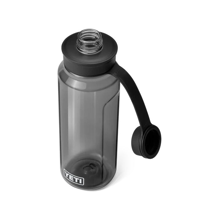 Die YETI® Yonder™ 1L Wasserflasche aus transparentem grauem Material ist BPA-frei und bruchfest, hat einen weiten Mund, einen schwarzen Schraubdeckel mit flexiblem Tragegriff; der Deckel liegt abgenommen neben der Flasche.
