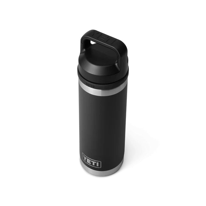 Die YETI® Flasche Rambler 18 Oz in Schwarz, mit doppelwandiger Vakuumisolierung, silbernem Boden, schwarzem Schraubdeckel und Griff, ist auf weißem Hintergrund mit dem YETI-Logo an der Seite und auf dem Deckel abgebildet.