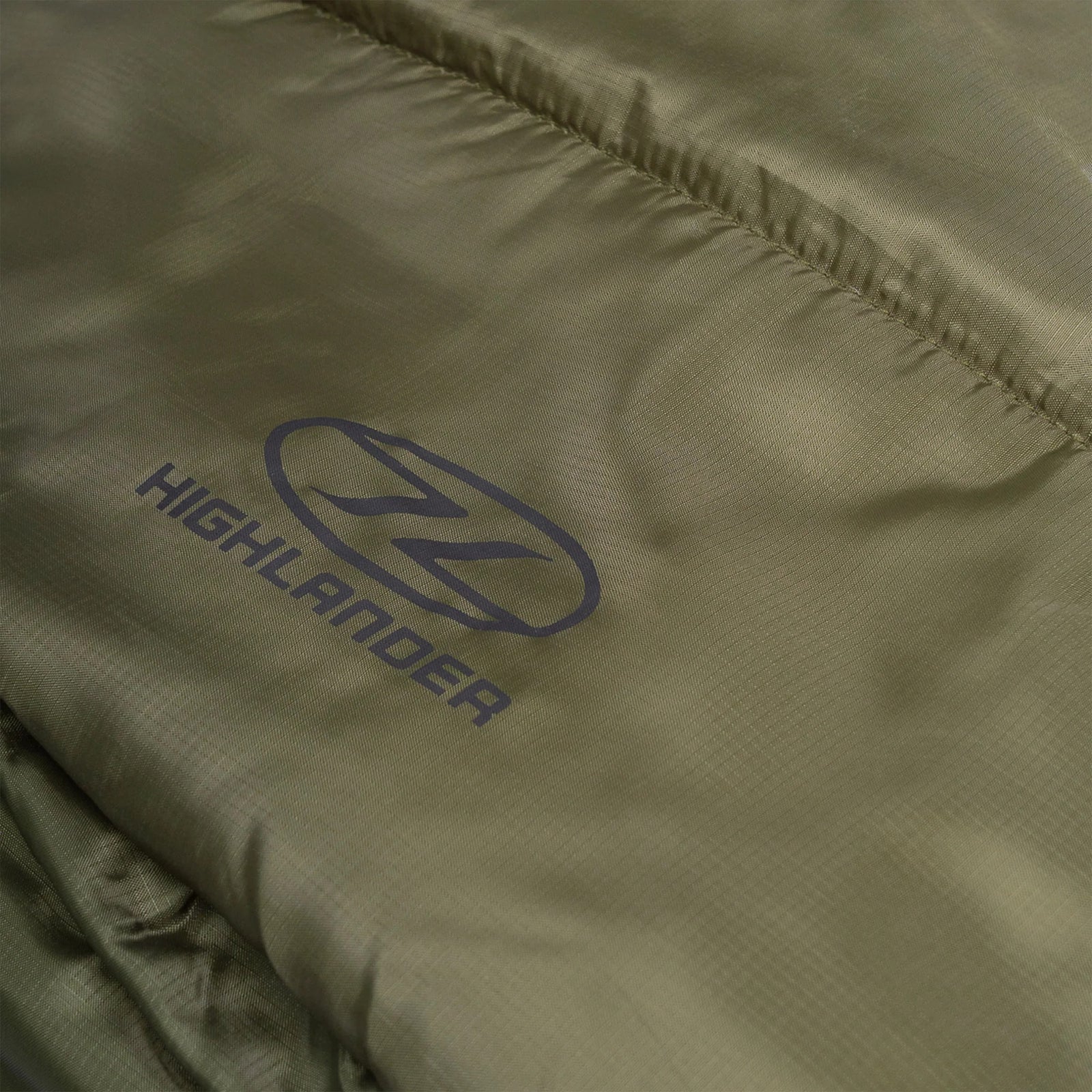 Nahaufnahme eines olivgrünen Stoffes mit dezentem Glanz, auf dem das HIGHLANDER OUTDOOR-Logo und der Name in Schwarz zu sehen sind. Dieses Material ist Teil des Highlander Schlafsacks Defender 450, der für den zuverlässigen Outdoor-Einsatz unter verschiedenen Bedingungen entwickelt wurde.