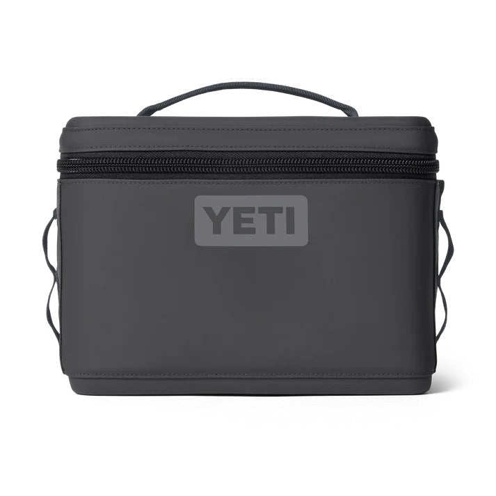 Die YETI® Kühltasche Daytrip 9L in Charcoal ist eine schwarze, rechteckige, isolierte Lunch-Tasche mit Reißverschluss, seitlichen Griffen und oberem Griff. Das YETI-Logo befindet sich auf der Vorderseite. Abgebildet vor einem weißen Hintergrund.