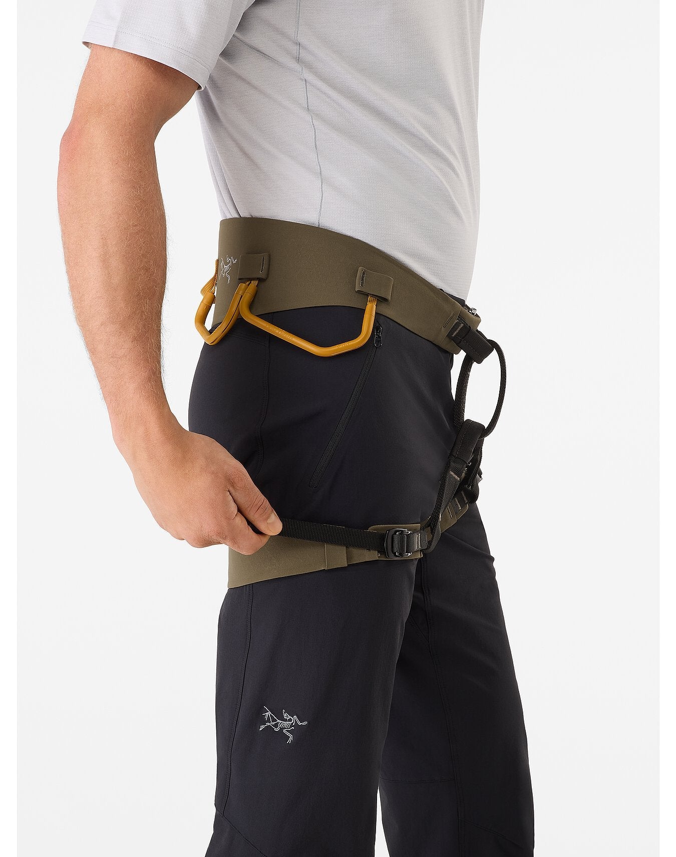 Eine Person in weißem Hemd und dunkler Hose stellt das ARC'TERYX LEAF Arc'teryx AR-395a Harness ein, das mit der Warp Strength Technology, gelben Materialschlaufen und einer Schnalle am Beingurt ausgestattet ist.