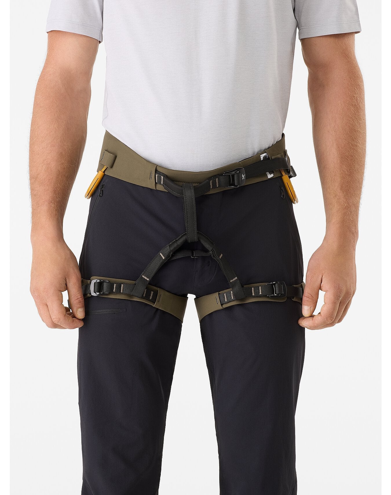 Eine Person in einem hellgrauen Hemd, dunkler Hose und einem ARC'TERYX LEAF Arc'teryx AR-395a Gurtzeug mit Schnallengurten und zwei gelben Werkzeugen daran. Der Kopf ist nicht sichtbar.