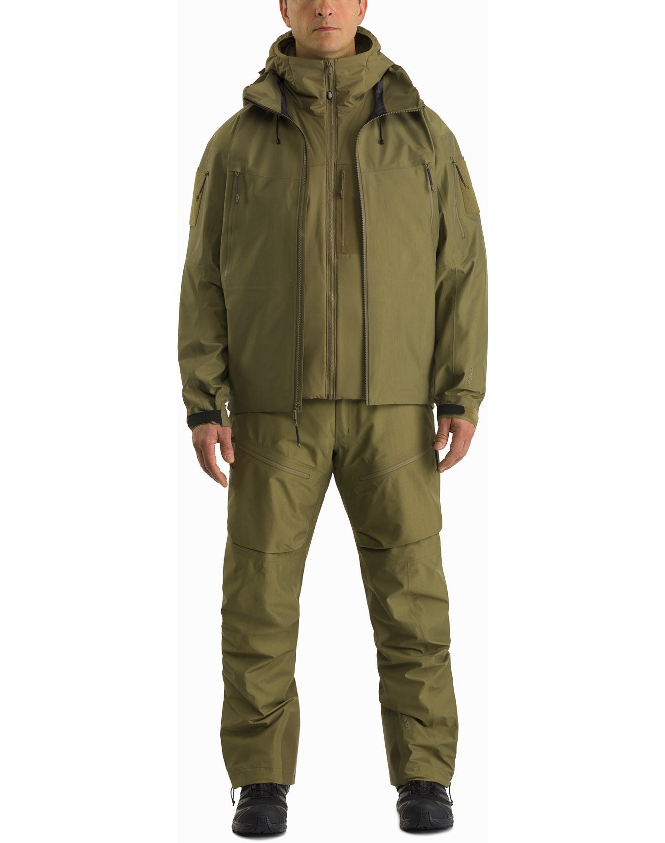 Eine Person, die einen ARC'TERYX LEAF Arc'teryx Atom Hoody LT Gen2.1 in Schwarz und eine dazu passende Cargohose trägt, steht mit Blick nach vorne, die Hände an den Seiten, in taktischer Kleidung und schwarzen Schuhen vor einem weißen Hintergrund.
