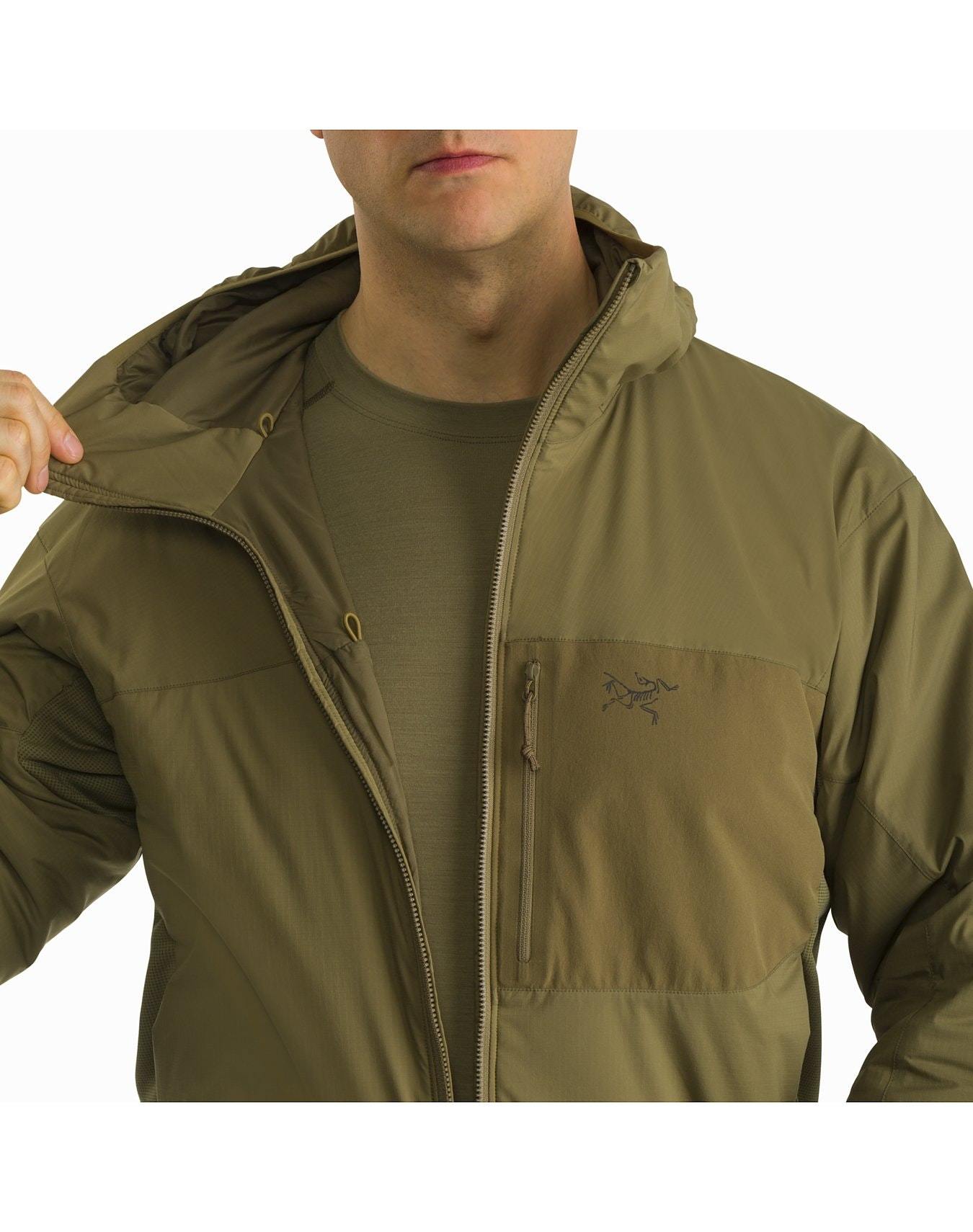 Eine Person, die eine olivgrüne ARC'TERYX LEAF Atom Hoody LT Gen2.1 - Crocodile über einem passenden T-Shirt trägt, öffnet teilweise den Reißverschluss der Jacke, um eine Brusttasche mit Reißverschluss und einem kleinen gestickten Logo freizulegen. Ihr Gesicht ist teilweise außerhalb des Rahmens.
