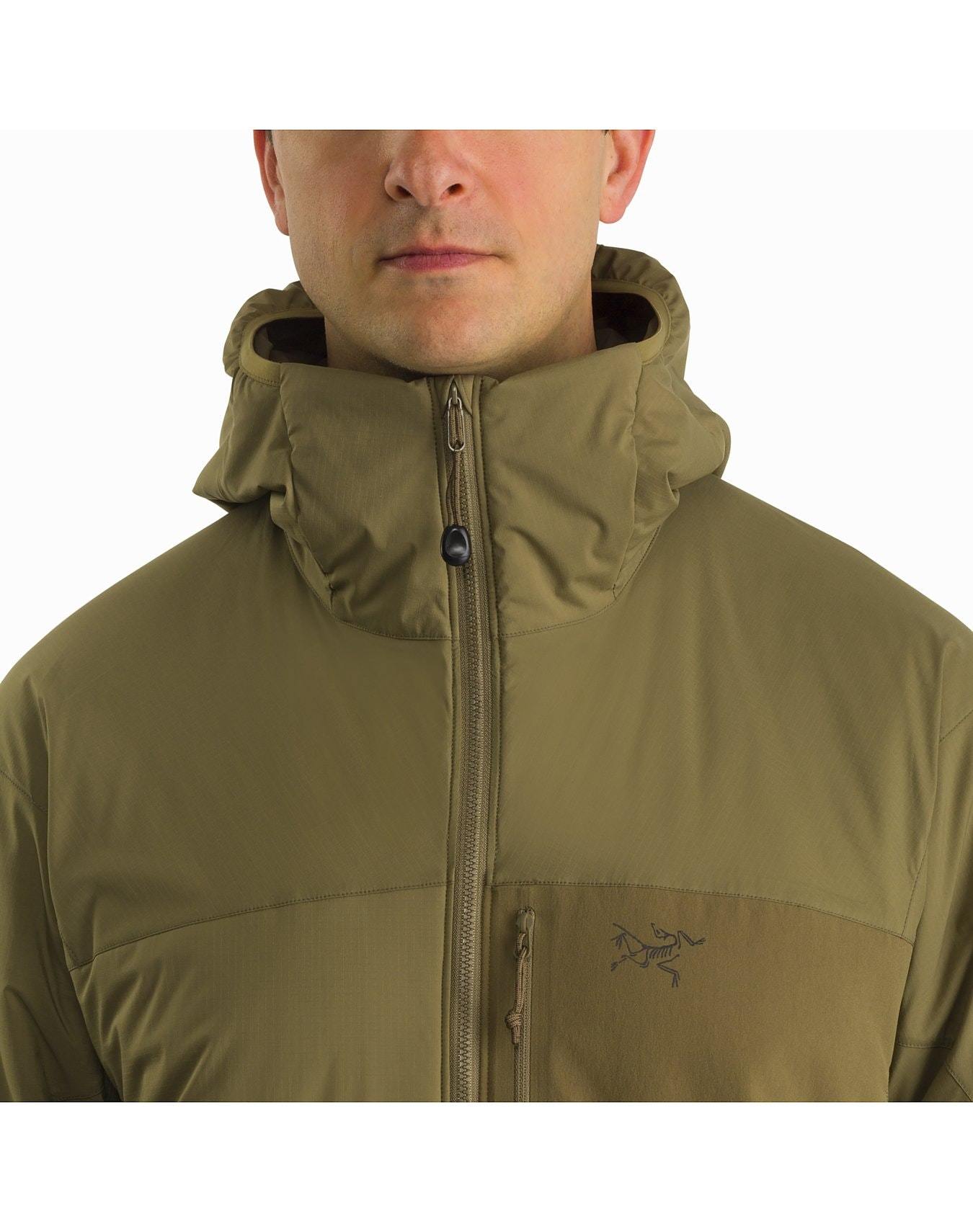 Eine Person trägt einen olivgrünen Arc'teryx Atom Hoody LT Gen2.1 - Crocodile von ARC'TERYX LEAF, dessen Reißverschluss nur die untere Hälfte des Gesichts und den oberen Teil des Oberkörpers zeigt. Die leichte Jacke hat ein kleines gesticktes Logo auf der linken Brust.