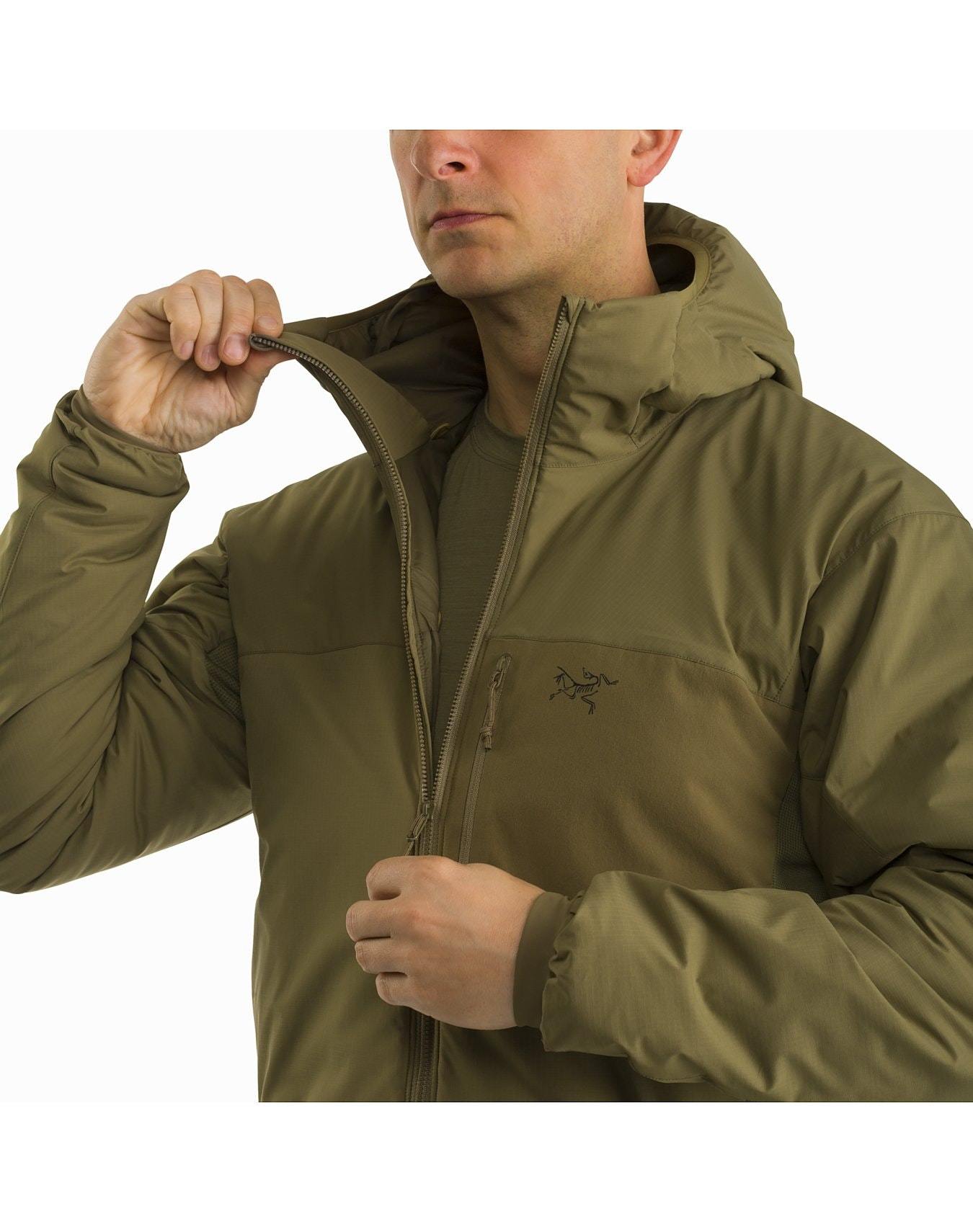 Eine Person, die ein ARC'TERYX LEAF Atom Hoody LT Gen2.1 in Ranger Green trägt, öffnet teilweise den Reißverschluss dieser leichten Isolationsjacke, wobei der Oberkörper im Mittelpunkt steht und das Logo und die Details hervorgehoben werden.