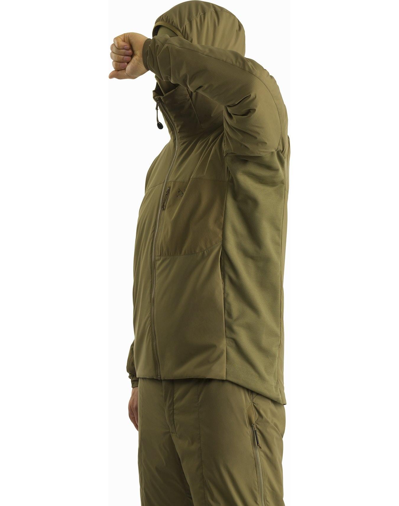 Jemand in einem wolfsfarbenen ARC'TERYX LEAF Arc'teryx Atom Hoody LT Gen2.1 steht seitlich, den rechten Arm über dem Gesicht verschränkt. Diese leichte Kapuzenjacke hat Reißverschlusstaschen, einen hohen Kragen und eine wärmende CLIMASHIELD-Isolierung.