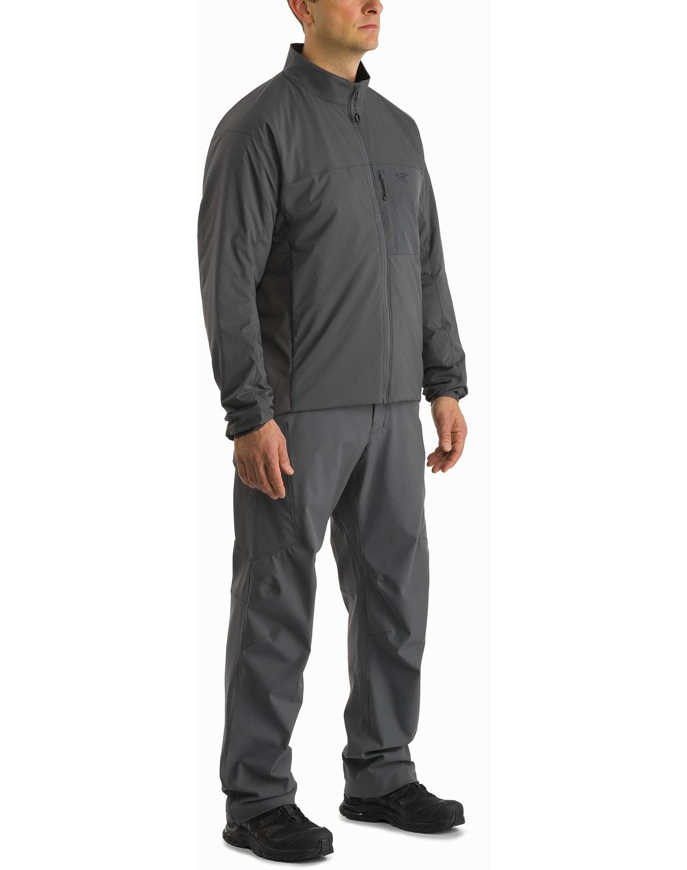 Ein Mann in einer passenden Arc'teryx Atom Jacket LT Gen2.1 - Ranger Green von ARC'TERYX LEAF und einer Hose mit schwarzen Turnschuhen, die zu drei Vierteln vor einem weißen Hintergrund gezeigt wird, zeigt den fortschrittlichen Komfort des POLARTEC Power Stretch-Gewebes.