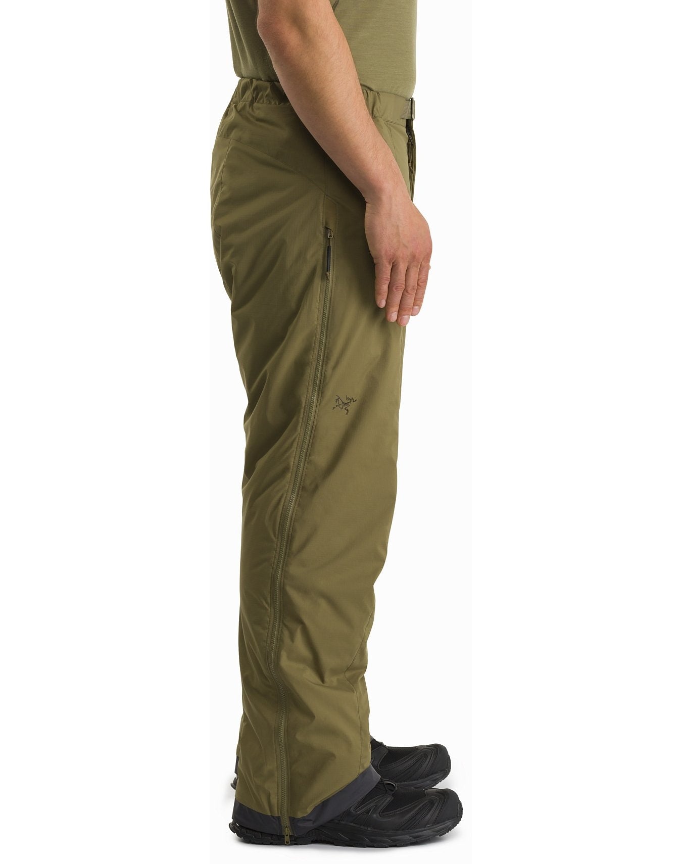 Eine Person im Profil trägt die ARC'TERYX LEAF Arc'teryx Atom Pant LT Gen2- Crocodile und schwarze Schuhe vor einem weißen Hintergrund. Diese leichte Outdoor-Hose hat einen seitlichen Reißverschluss und scheint aus strapazierfähigem Stoff zu bestehen.