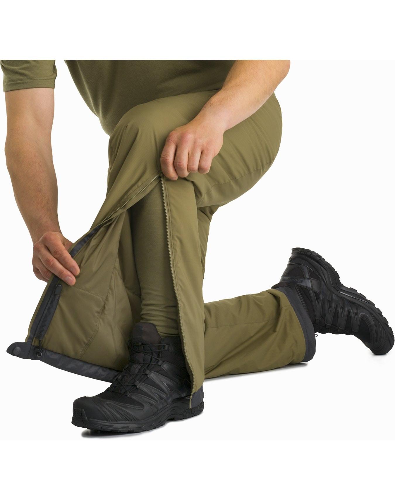Eine Person kniet sich hin und öffnet den Reißverschluss an der Seite der schwarzen ARC'TERYX LEAF Arc'teryx Atom Pant LT Gen2 über den Wanderschuhen, um den seitlichen Reißverschluss zur Belüftung oder zum leichteren Ausziehen freizulegen.