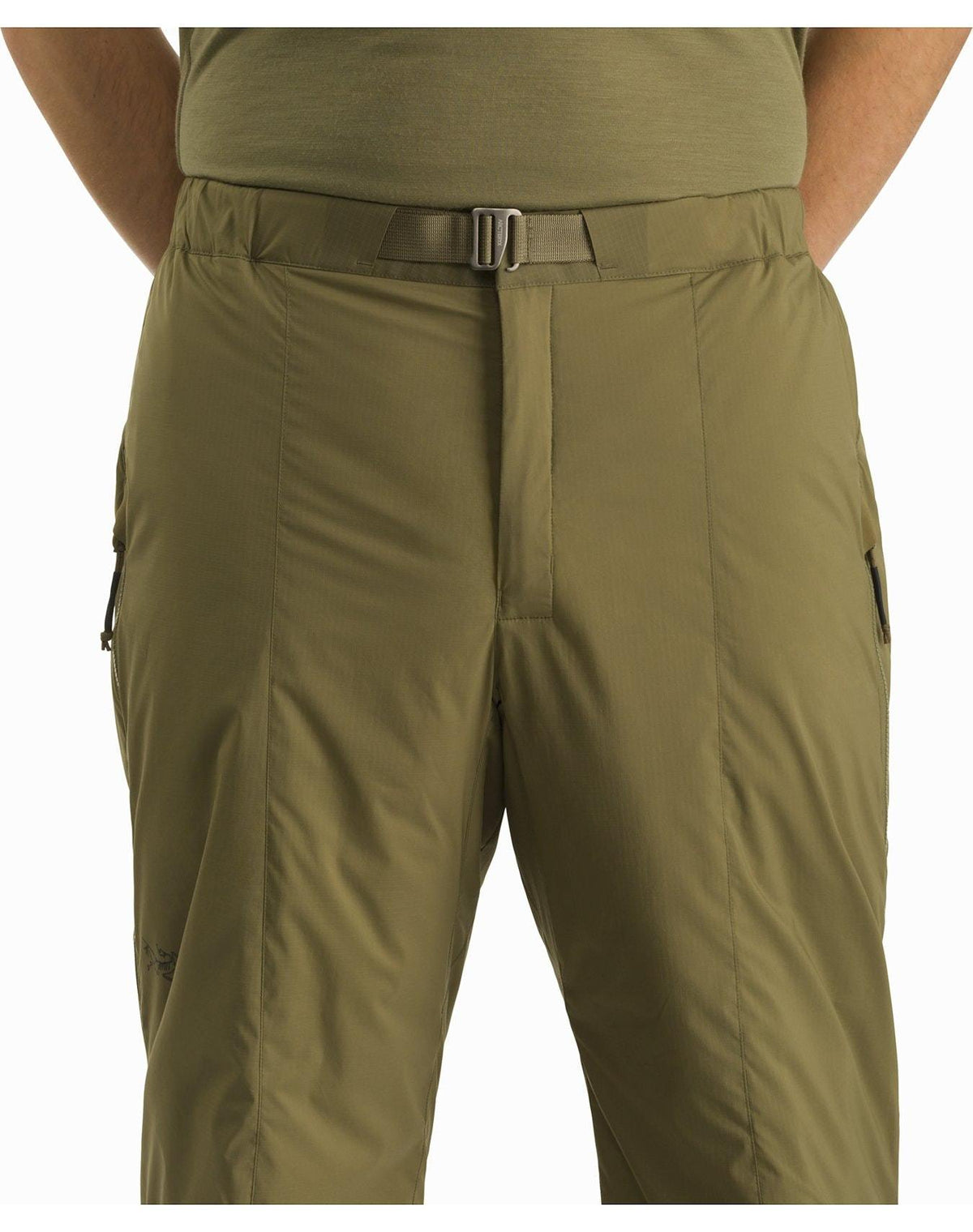 Eine Person trägt die ARC'TERYX LEAF Arc'teryx Atom Pant LT Gen2 in Schwarz mit einem schmalen Gürtel und einem grünen Hemd, dargestellt von der Taille bis zur Mitte des Oberschenkels. Die Hände ruhen in den seitlichen Reißverschlusstaschen, was den funktionellen Stil der Hose unterstreicht.