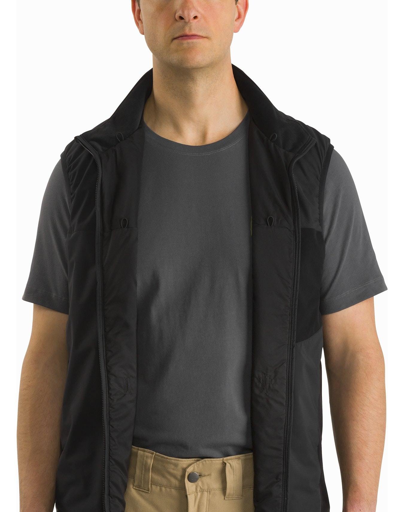 Ein Mann trägt eine ARC'TERYX LEAF Atom Vest LT Gen2.1 - Wolf über einem dunkelgrauen T-Shirt und einer hellbraunen Hose. Er steht vor einem weißen Hintergrund, sein Gesicht ist teilweise sichtbar und seine Arme sind entspannt an seinen Seiten.