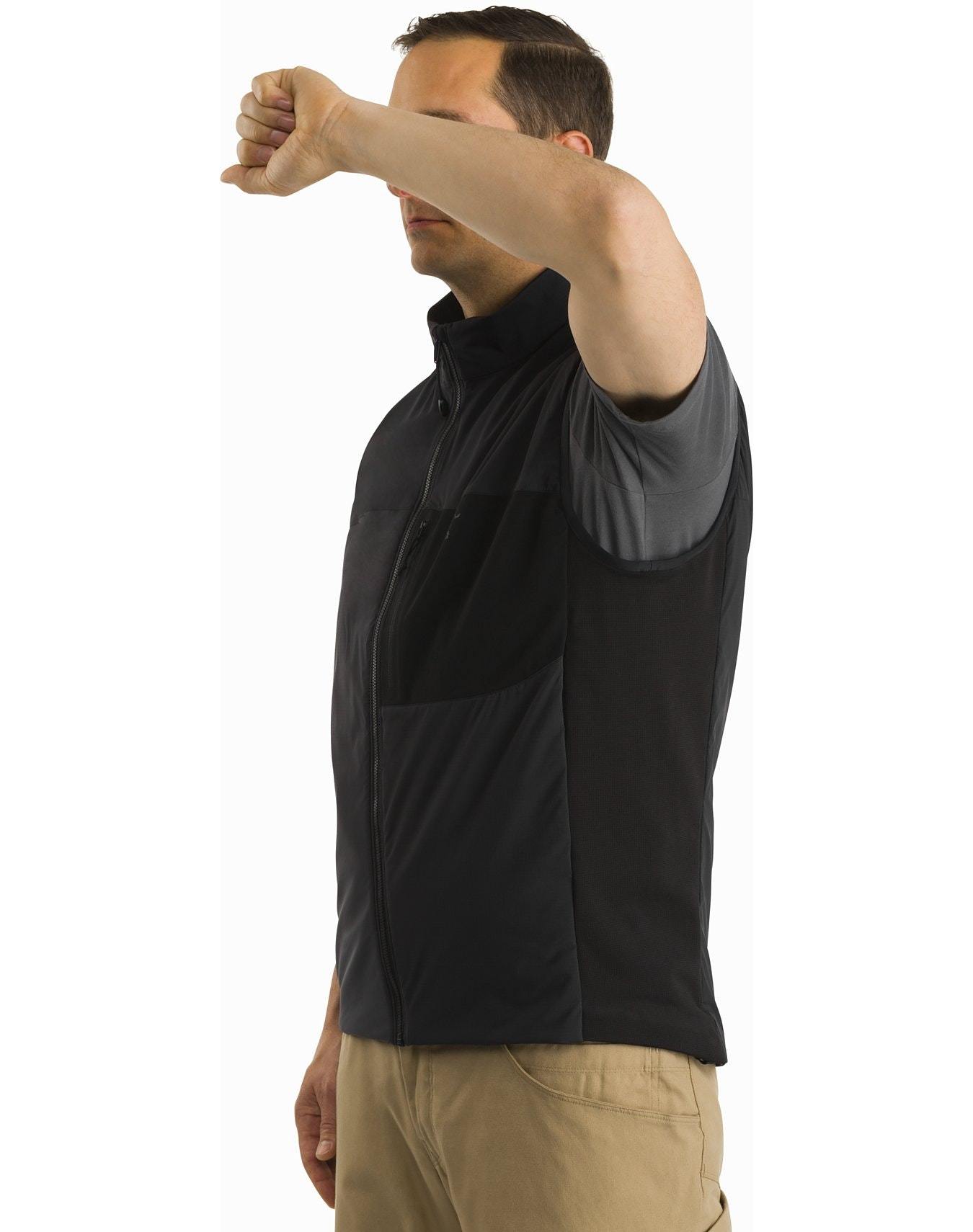 Ein Mann in einer ARC'TERYX LEAF Arc'teryx Atom Vest LT Gen2.1 - Wolf, grauem Hemd und khakifarbener Hose steht seitlich, den rechten Arm angewinkelt und den Unterarm angehoben, um sein Gesicht teilweise zu verdecken.