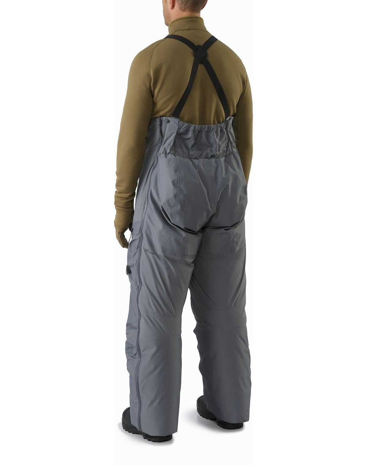 Eine Person, die die ARC'TERYX LEAF Arc'teryx Cold WX Bib Pant SVX Men's - Harrier mit schwarzen Hosenträgern und einem braunen langärmeligen Hemd trägt, wird von hinten vor einem weißen Hintergrund gezeigt.