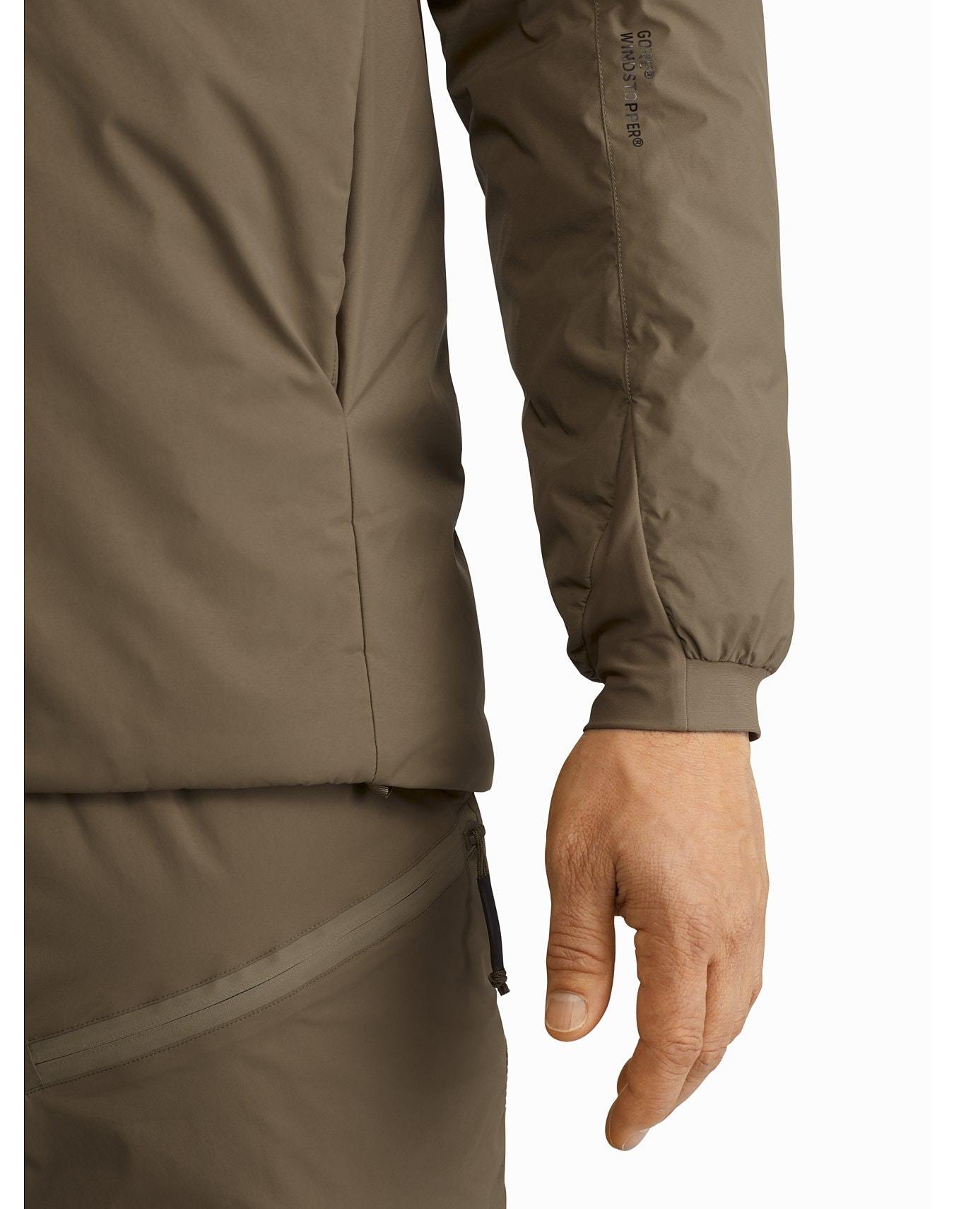 Nahaufnahme einer Person, die den ARC'TERYX LEAF Arc'teryx Cold WX Hoody LT Gen2.1 in Ranger Green trägt. Hervorzuheben sind die gerippten Bündchen, die Seitennähte und die passende Hose mit sichtbarer Reißverschlusstasche.