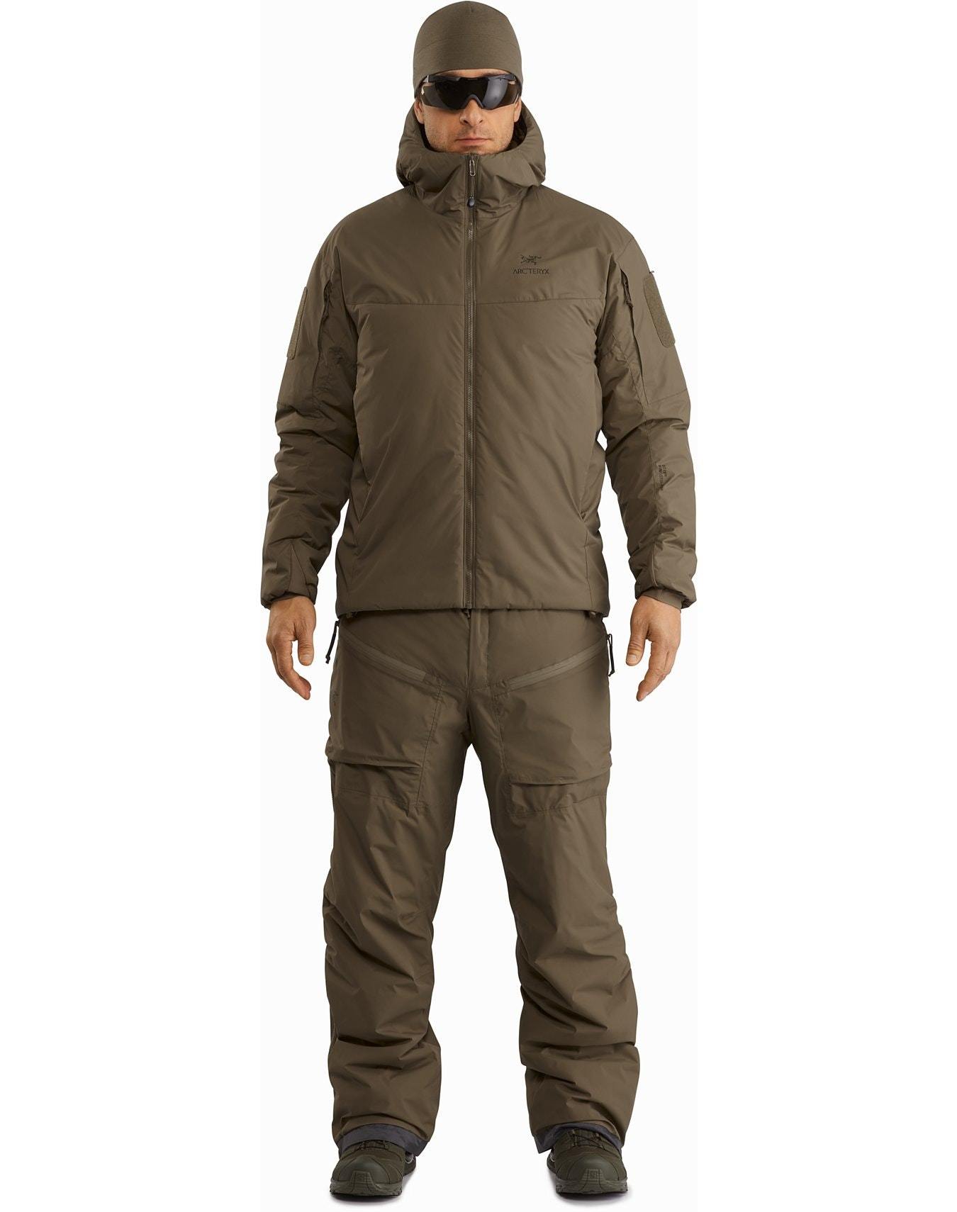 Ein Mann trägt den ARC'TERYX LEAF Cold WX Hoody LT Gen2.1 in Ranger Green mit isolierter Kapuze, passender taktischer Hose, Sonnenbrille und Mütze in einer Ganzkörper-Produktaufnahme von vorne.