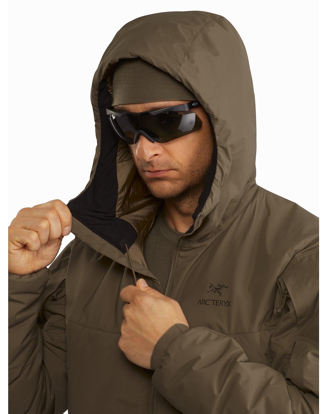 Ein Mann mit Sonnenbrille und Stirnband schließt den Reißverschluss an der Vorderseite eines ARC'TERYX LEAF Arc'teryx Cold WX Hoody LT Gen2.1 in Ranger Green und verstellt die Kapuze.