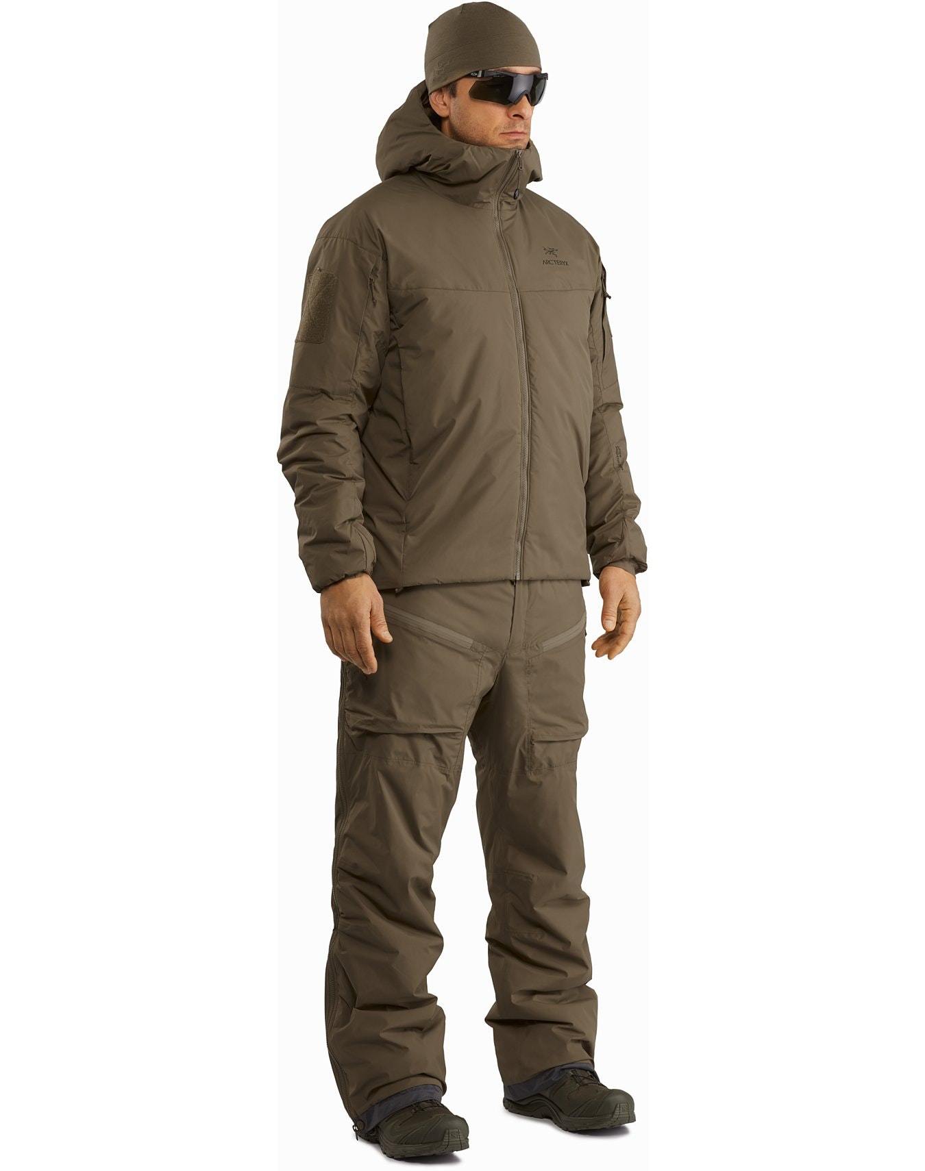 Eine Person trägt einen ARC'TERYX LEAF Cold WX Hoody LT Gen2.1 in Wolf mit einer passenden Hose, einer Mütze, einer Sonnenbrille und dunklen Schuhen - ein isoliertes Outfit, das ideal für kaltes Wetter oder Outdoor-Abenteuer ist.