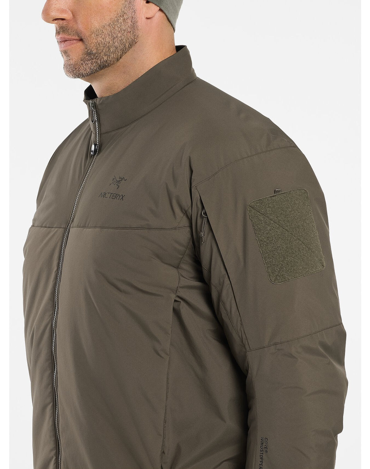 Ein Mann, der eine schwarze ARC'TERYX LEAF Cold WX Jacket LT Gen2.1 und eine passende Mütze trägt, wird von den Schultern aufwärts in einem leichten Winkel gezeigt. Die Jacke hat einen Reißverschluss vorne, einen Armaufnäher und ein dezentes Arc'teryx-Logo auf der Brust.