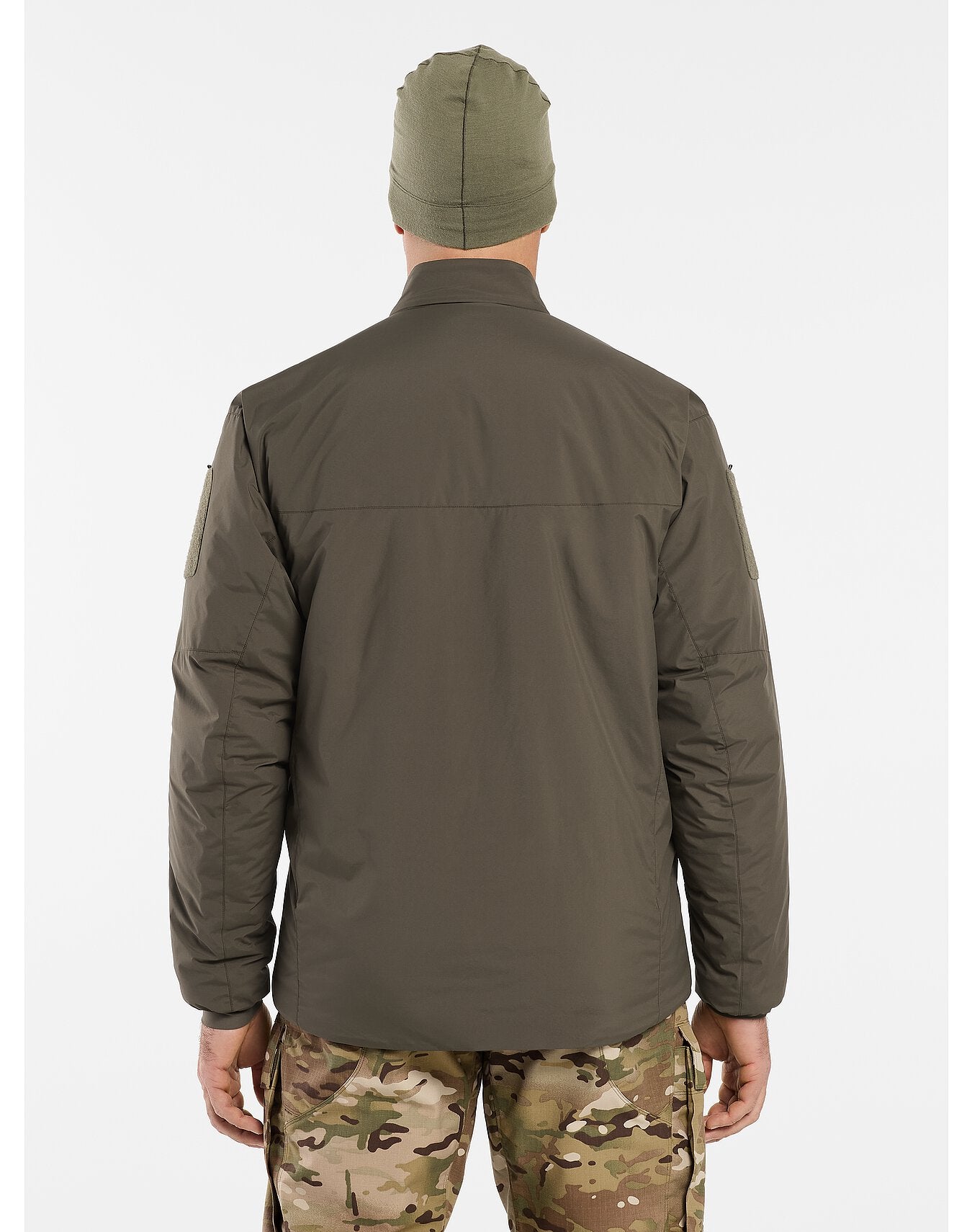 Eine Person, die eine olivgrüne Mütze, eine Tarnhose und eine ARC'TERYX LEAF Arc'teryx Cold WX Jacket LT Gen2.1 in Schwarz trägt, steht mit dem Rücken zur Kamera vor einem schlichten weißen Hintergrund.
