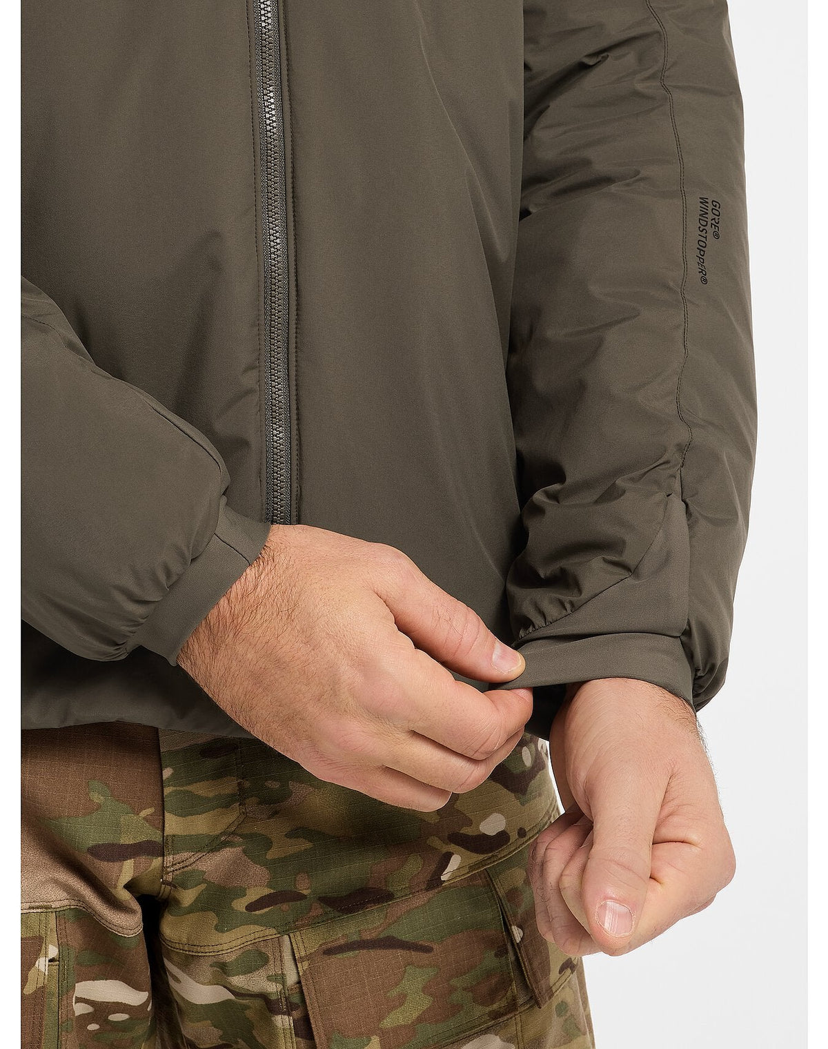 Eine Person, die eine ARC'TERYX LEAF Arc'teryx Cold WX Jacket LT Gen2.1 in Ranger Green und eine Camouflage-Hose trägt, verstellt den Ärmel ihrer Jacke mit einer Hand.