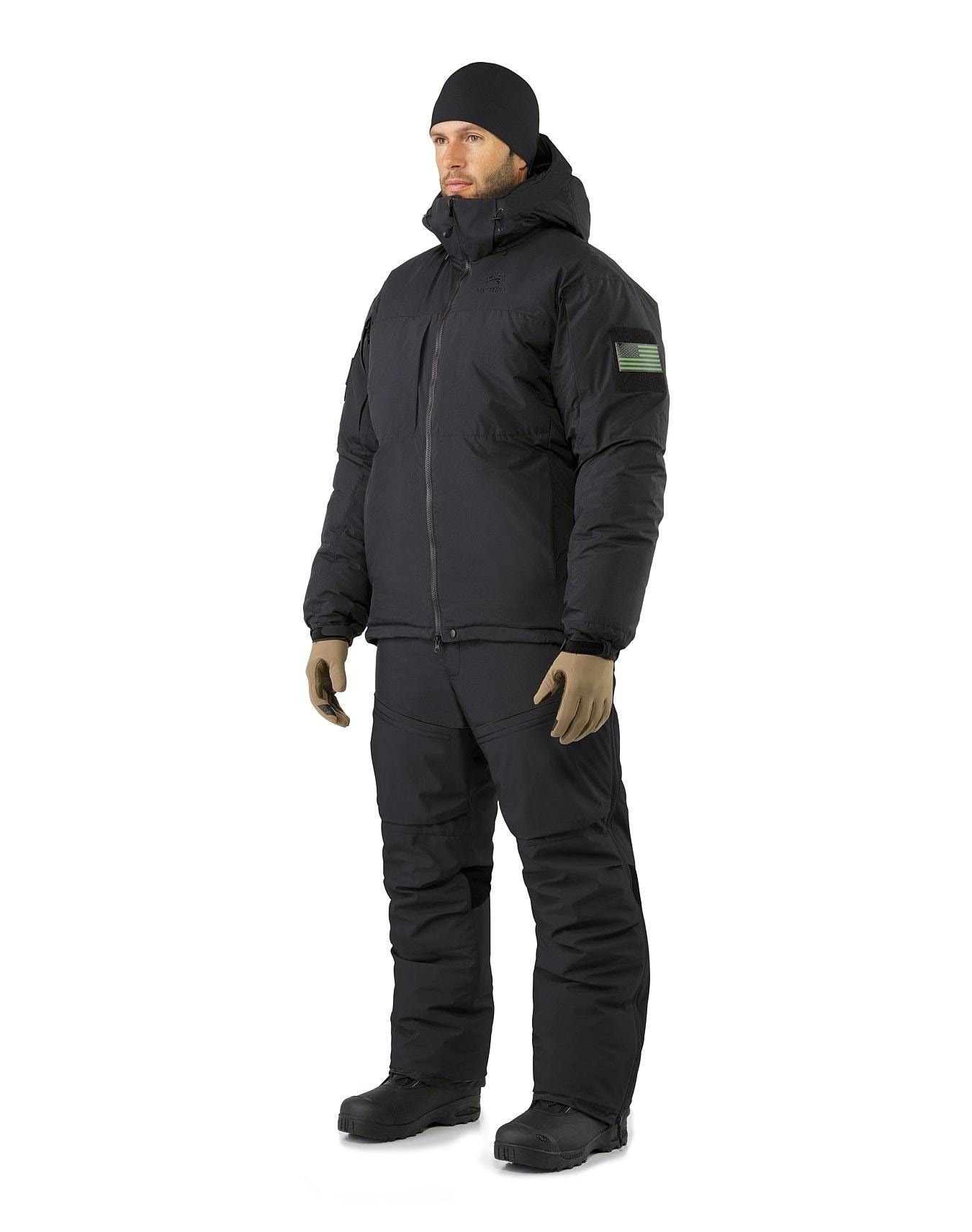 Eine Person, die eine ARC'TERYX LEAF Arc'teryx Cold WX Jacket SV Gen1.4 und eine Hose mit einer schwarzen Mütze, hellbraunen Handschuhen und schwarzen Stiefeln trägt, steht vor einem einfarbig weißen Hintergrund.