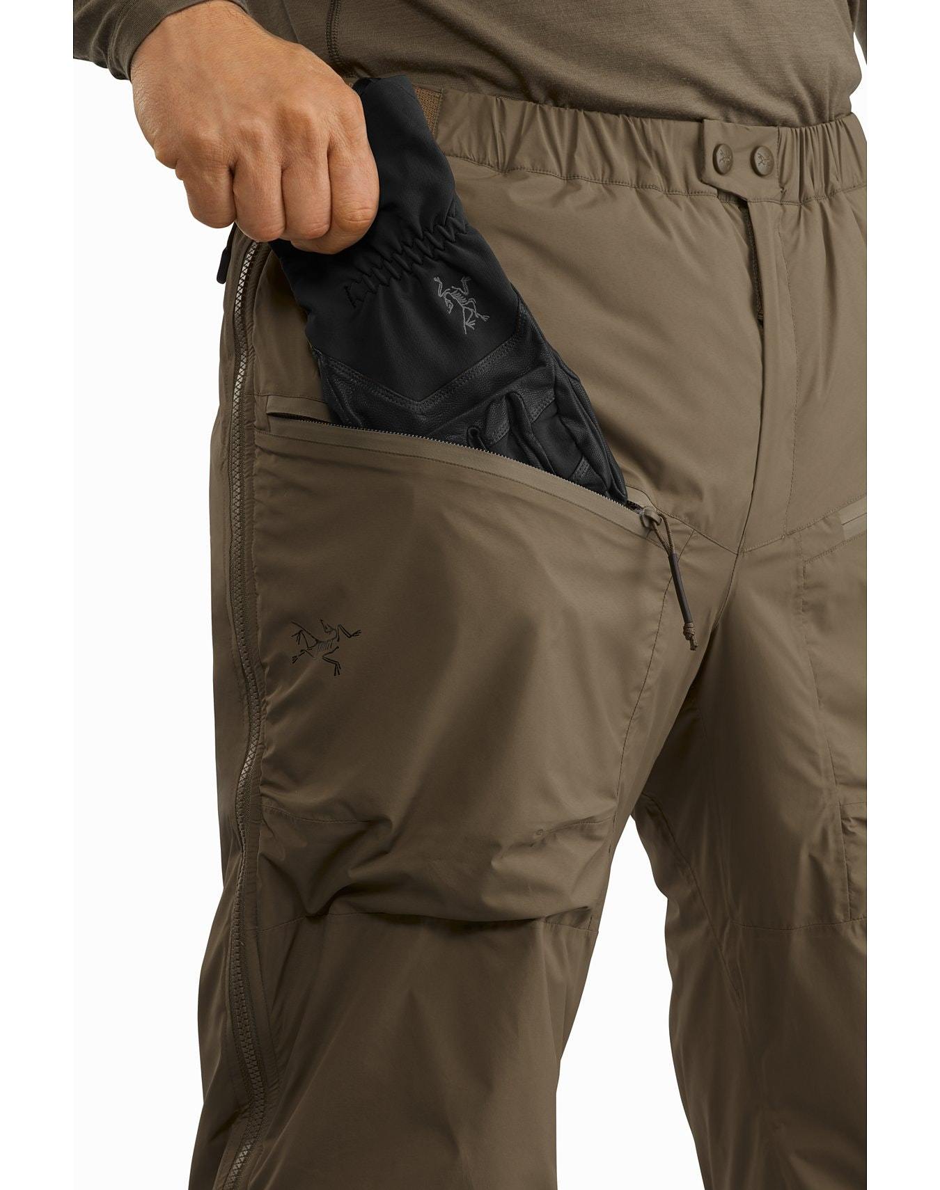 Eine Person in der Arc'teryx Cold WX Pant LT Gen2 - Black von ARC'TERYX LEAF öffnet die große Seitentasche, um schwarze Handschuhe zu verstauen. Diese taktische Hose für kaltes Wetter hat einen Knopfverschluss und ein sichtbares ARC'TERYX LEAF-Logo in der Nähe der Tasche.