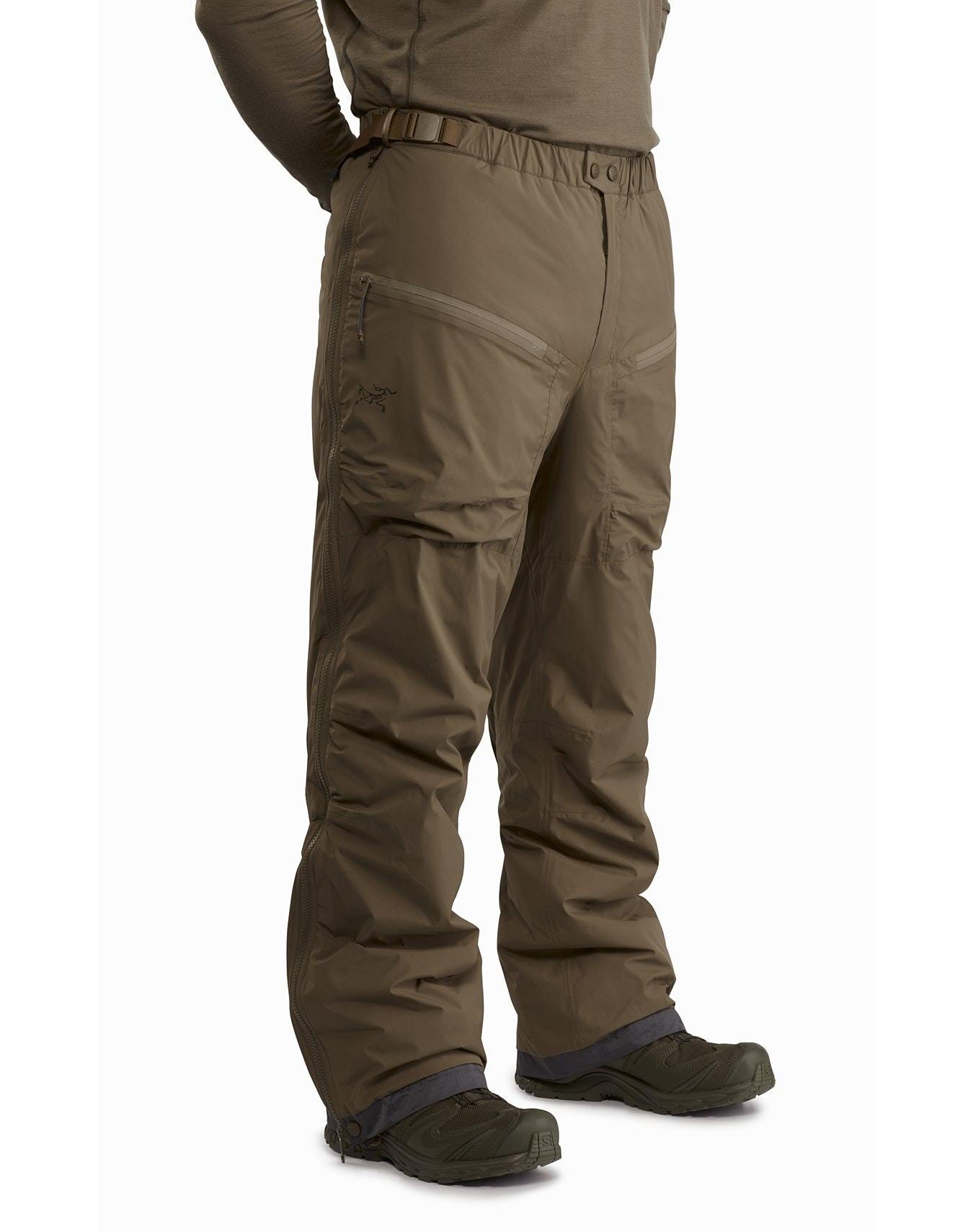 Eine Person trägt ARC'TERYX LEAF Arc'teryx Cold WX Pant LT Gen2 - Crocodile wasserdichte Hose und dunkle Schuhe, steht mit den Händen auf dem Rücken; nur der Unterkörper ist vor einem weißen Hintergrund zu sehen.