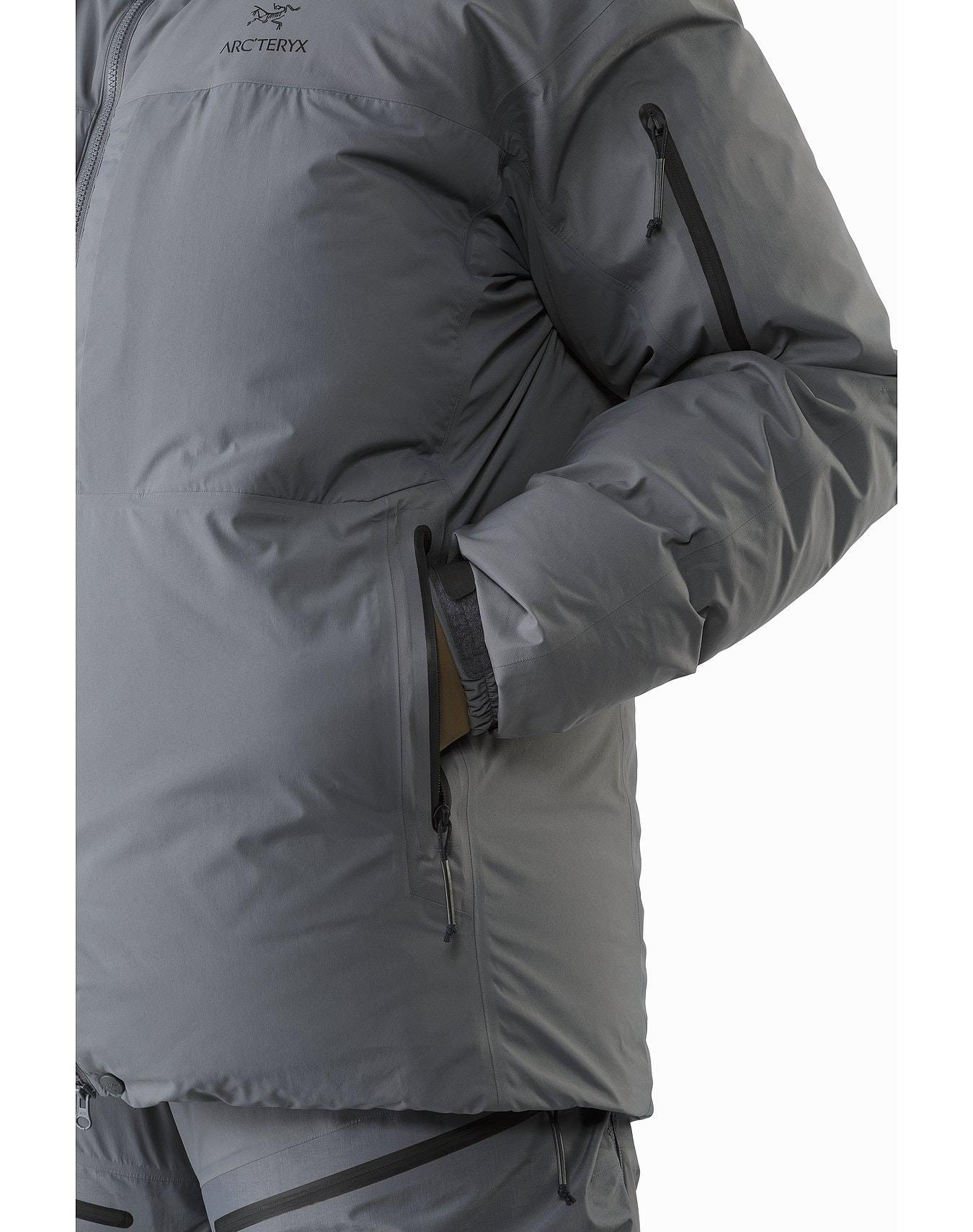 Seitenansicht der ARC'TERYX LEAF Arc'teryx Cold WX Parka SVX - Wolf, einer grauen, isolierten Herrenjacke mit Reißverschlusstaschen auf der Brust und der Hüfte, wobei der Arm über dem Körper gekreuzt wird.