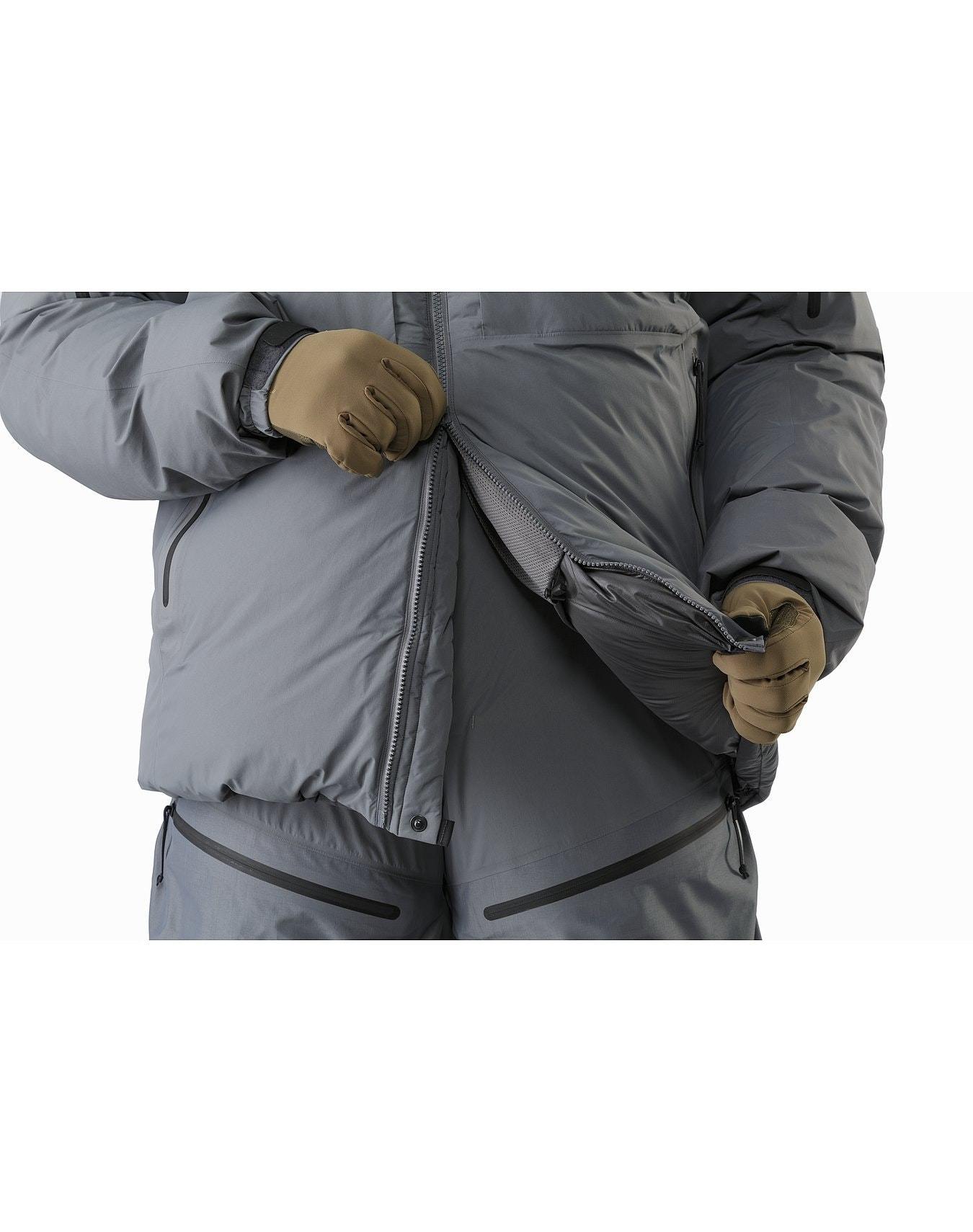 Eine Person öffnet die Vorderseite eines Arc'teryx Cold WX Parka SVX - Wolf von ARC'TERYX LEAF und trägt dabei braune Handschuhe. Das Foto ist so beschnitten, dass nur ihr Oberkörper und ihre Oberschenkel zu sehen sind.