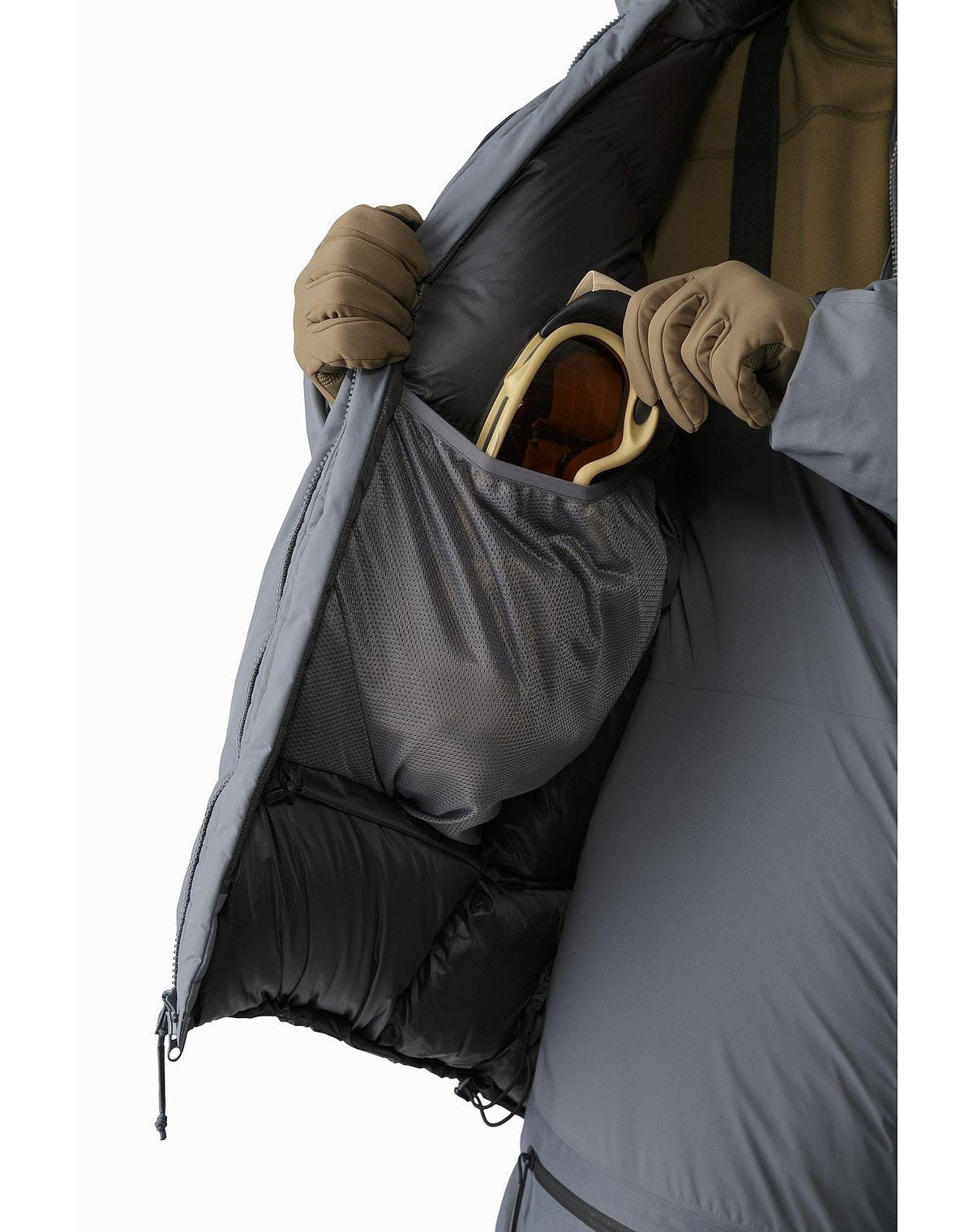 Nahaufnahme der grauen, isolierten Innenseite des ARC'TERYX LEAF Arc'teryx Cold WX Parka SVX - Wolf. Sie zeigt eine große Netztasche für Skibrillen, die mit Handschuhen geöffnet werden kann und Wärme und sichere Aufbewahrung auf der Piste bietet.