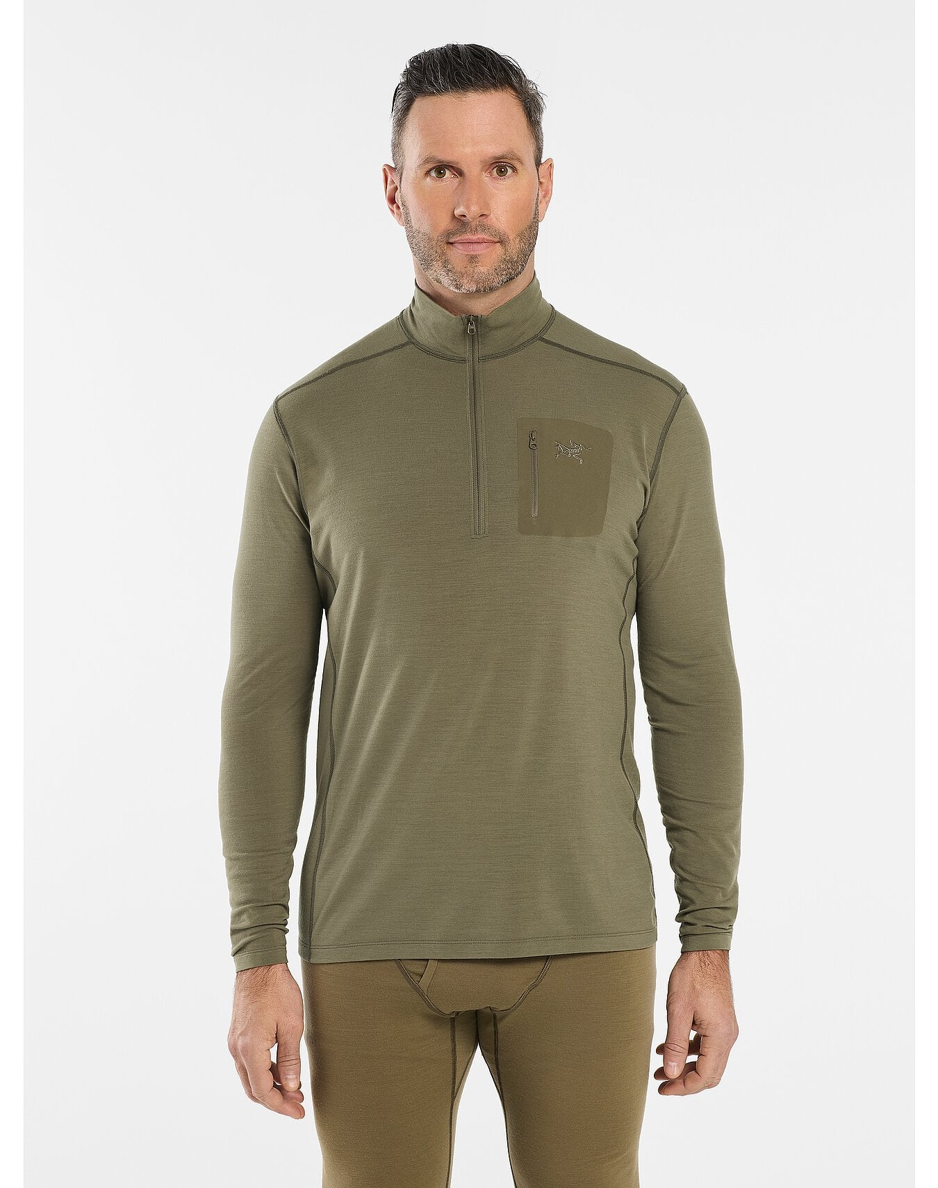 Mann trägt eine ARC'TERYX LEAF Cold WX Zip Neck AR Basisschicht in Schwarz mit einer Reißverschlusstasche auf der Brust und einem Logoaufnäher, hergestellt aus Merinowolle, gepaart mit einer passenden Thermohose.